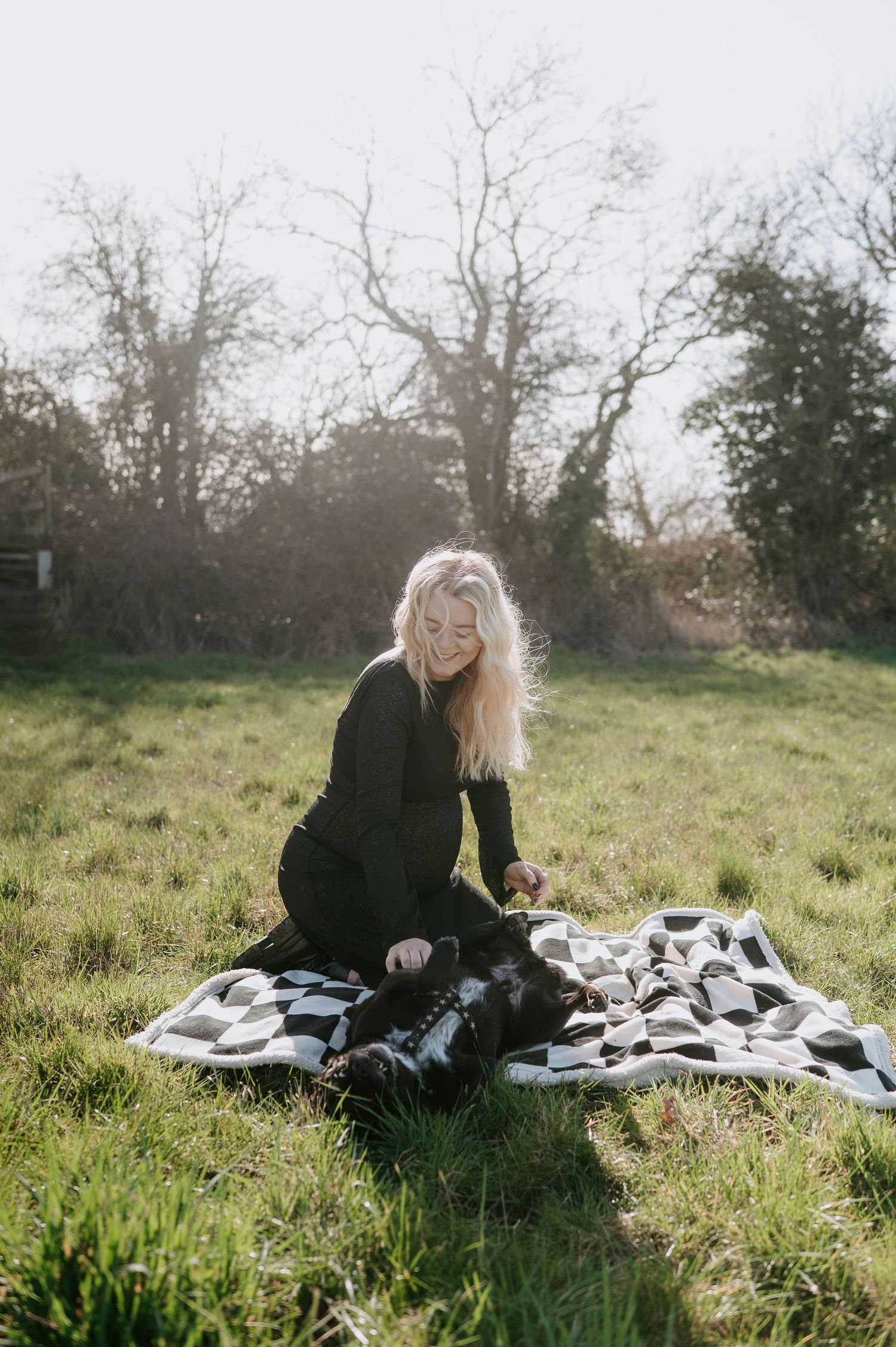 A person in black clothing relaxes on a blanket in a sunny meadow with scattered papers on a spring day.