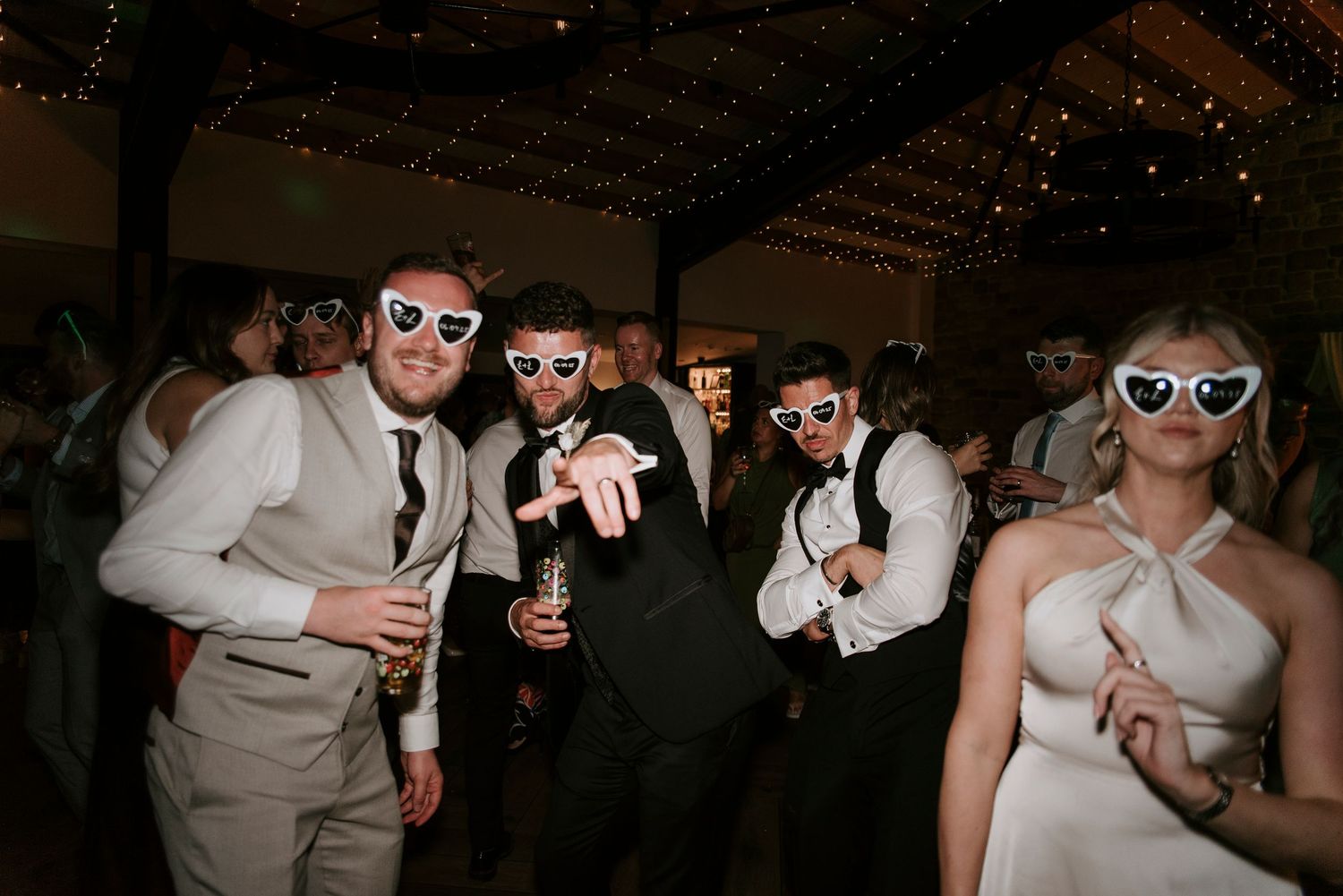 People dancing and celebrating at a lively party wearing sunglasses and formal attire.