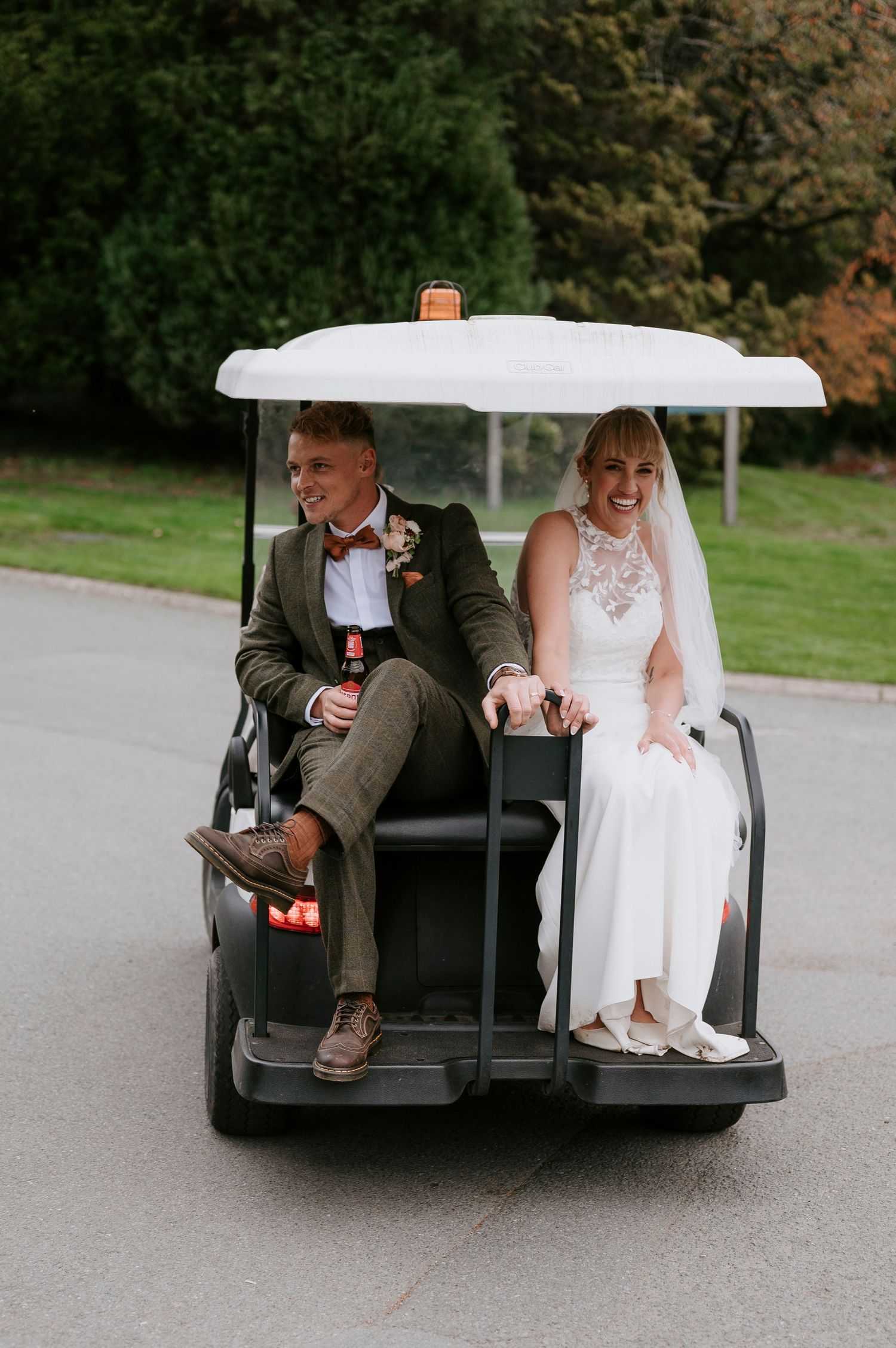 Newlywed couple riding in golf cart, bride in white dress and groom in dark suit laughing together.