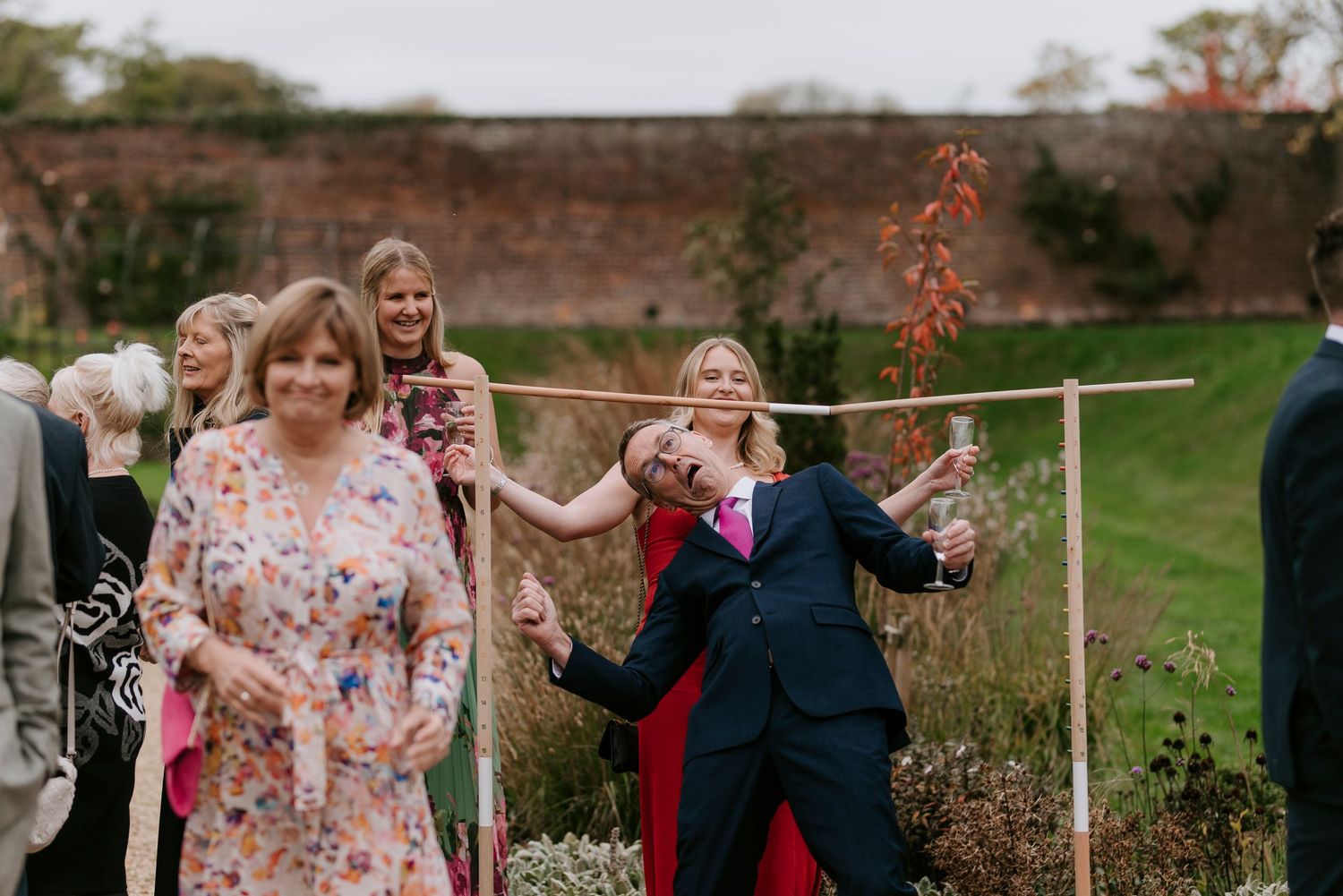 A group of people dancing in a garden setting with autumn foliage and white poles in the background.
