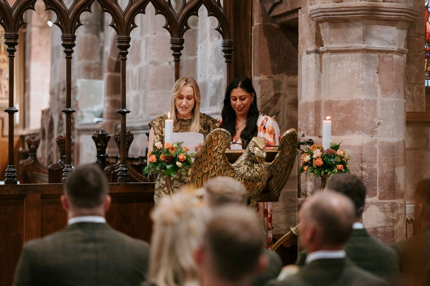 Two people seated at an ornate church altar with floral arrangements and guests in attendance during a ceremony.