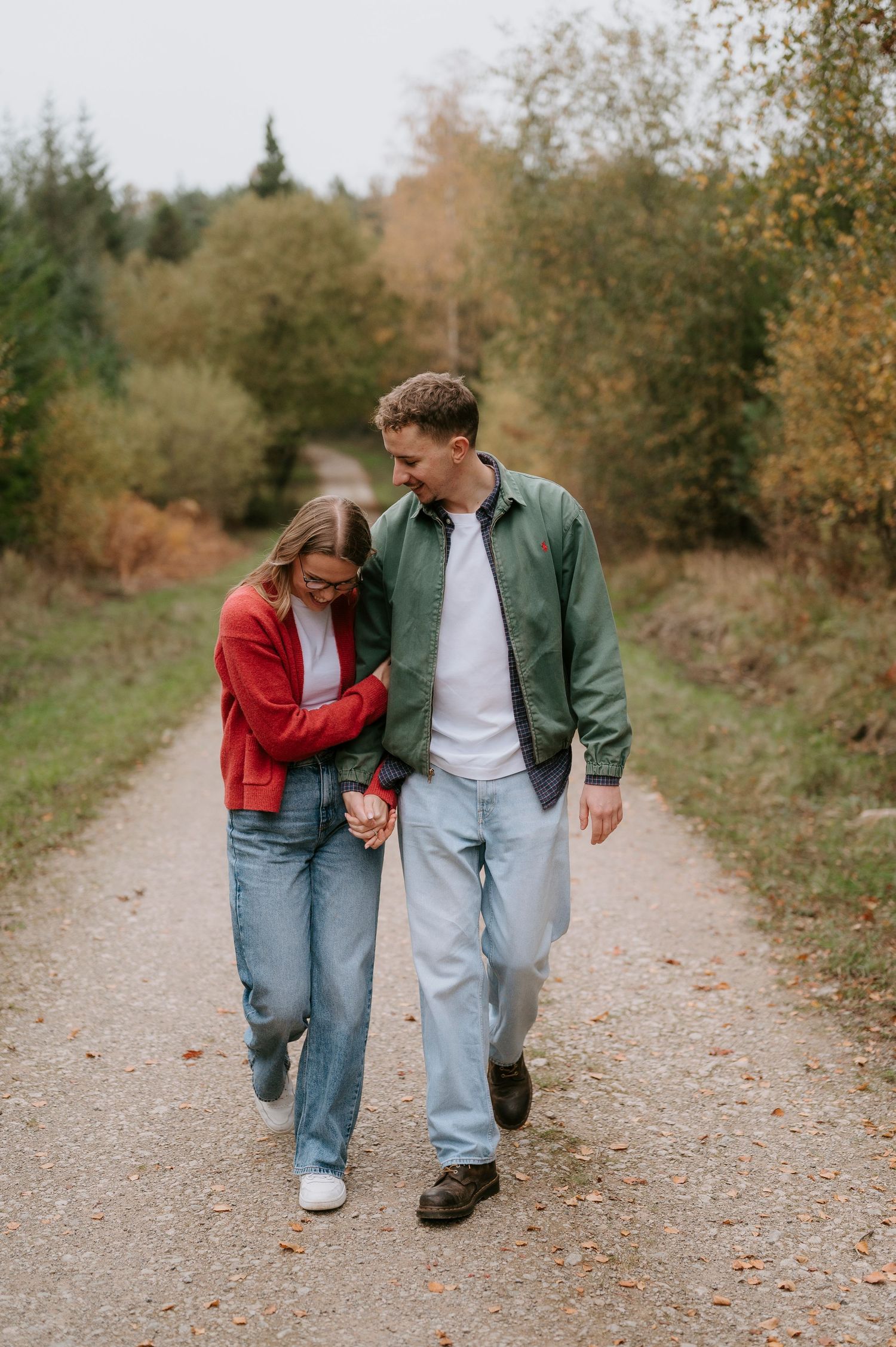 A couple walking together on a gravel path through autumn trees wearing casual denim and jackets.