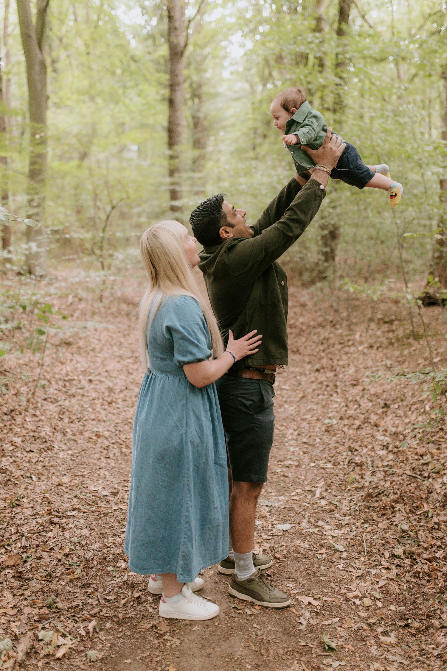 A family enjoys a playful moment together on a wooded trail surrounded by lush green trees on a spring day.