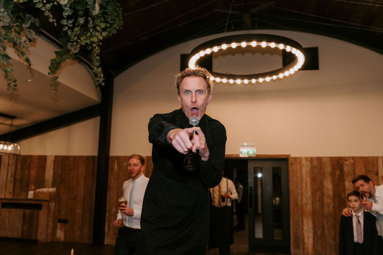 Wedding guests dance and celebrate on a wooden floor under ambient lighting during an evening reception.