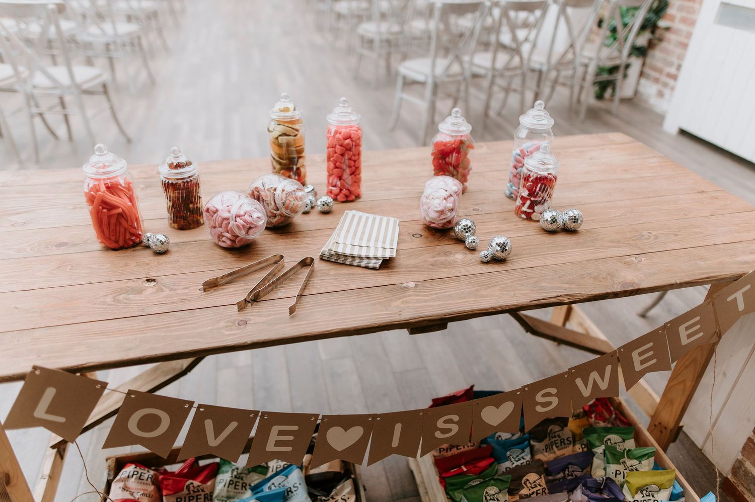 Glass candy jars filled with pink and red sweets displayed on wooden table with decorative banner below.
