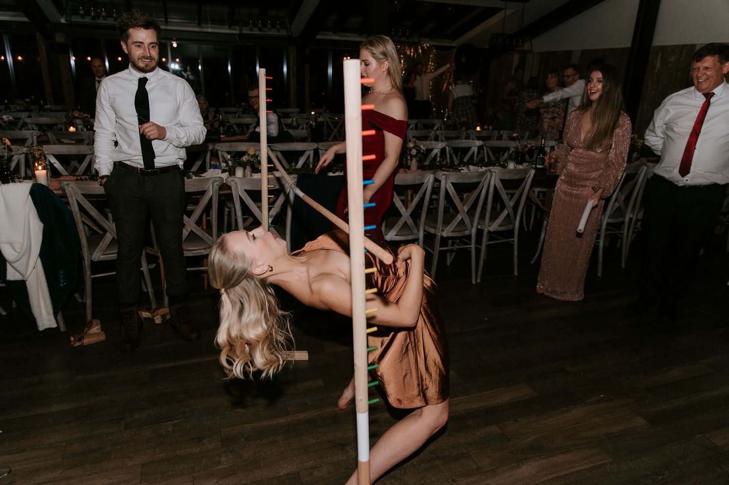 A dancer performs on a pole at a wedding reception while guests watch from the dance floor.