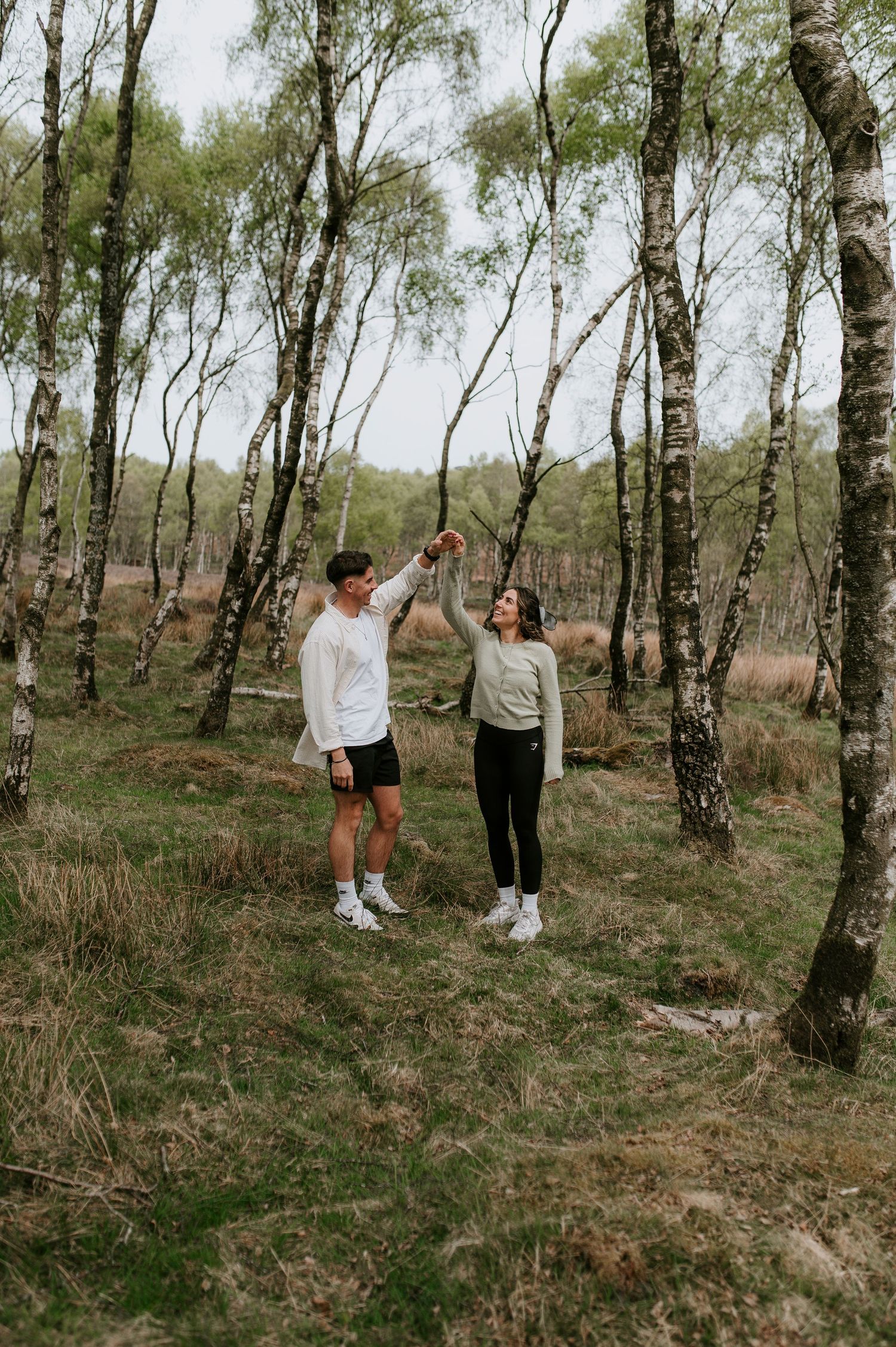A couple dancing and holding hands in a scenic birch forest on a cloudy day.