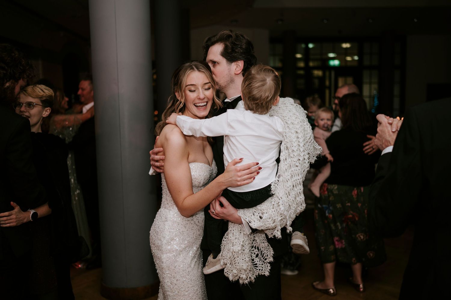 Wedding reception guests dancing and celebrating together in a dimly lit venue.