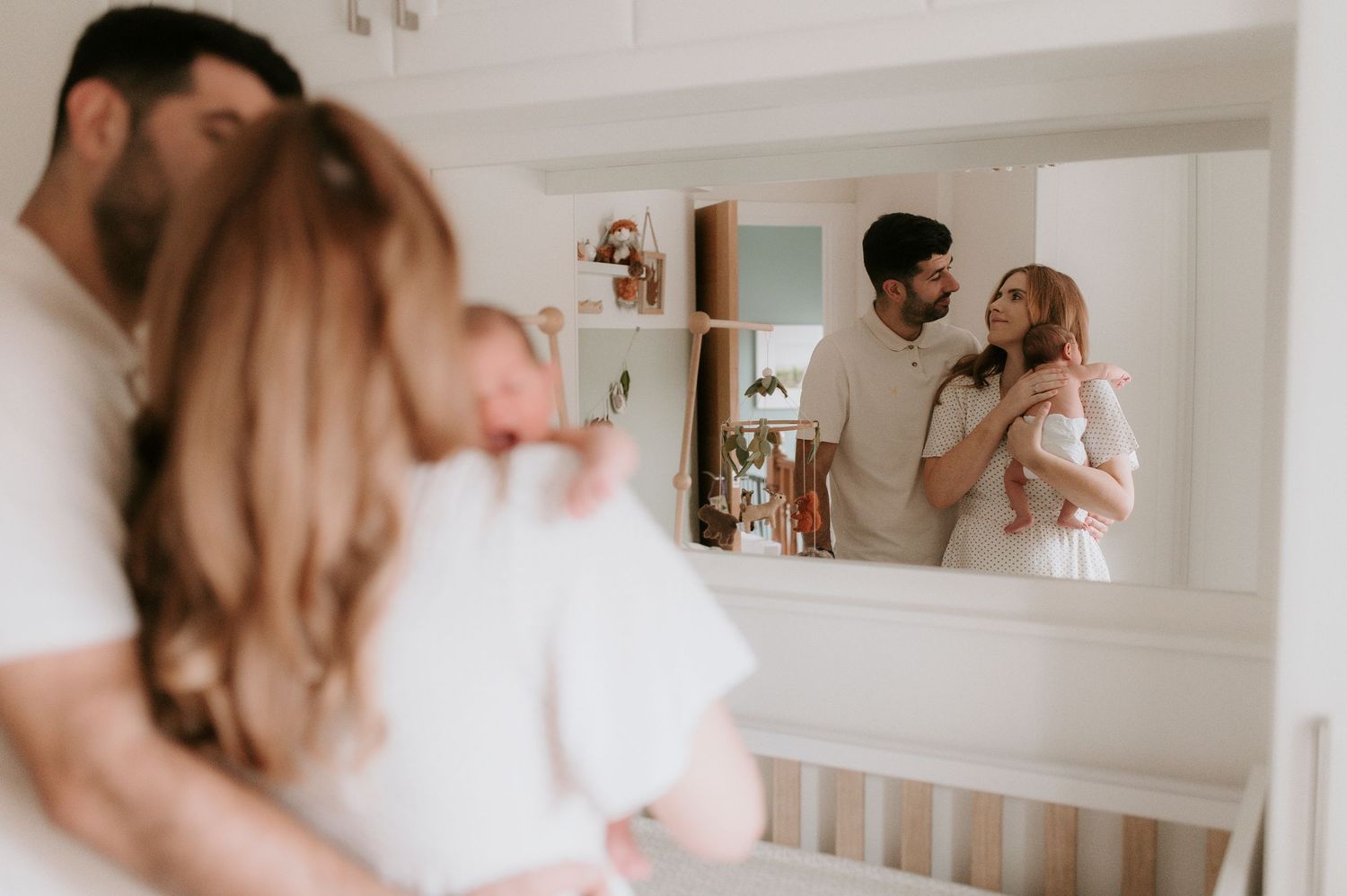 A couple embraces while looking at their reflection in a nursery mirror, creating a tender moment in soft lighting.