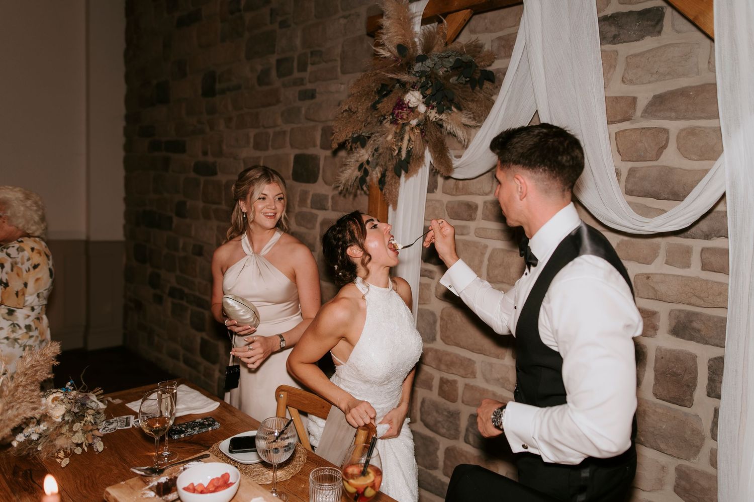 A joyful wedding reception moment captured at a rustic stone-walled venue with elegant decor and table settings.