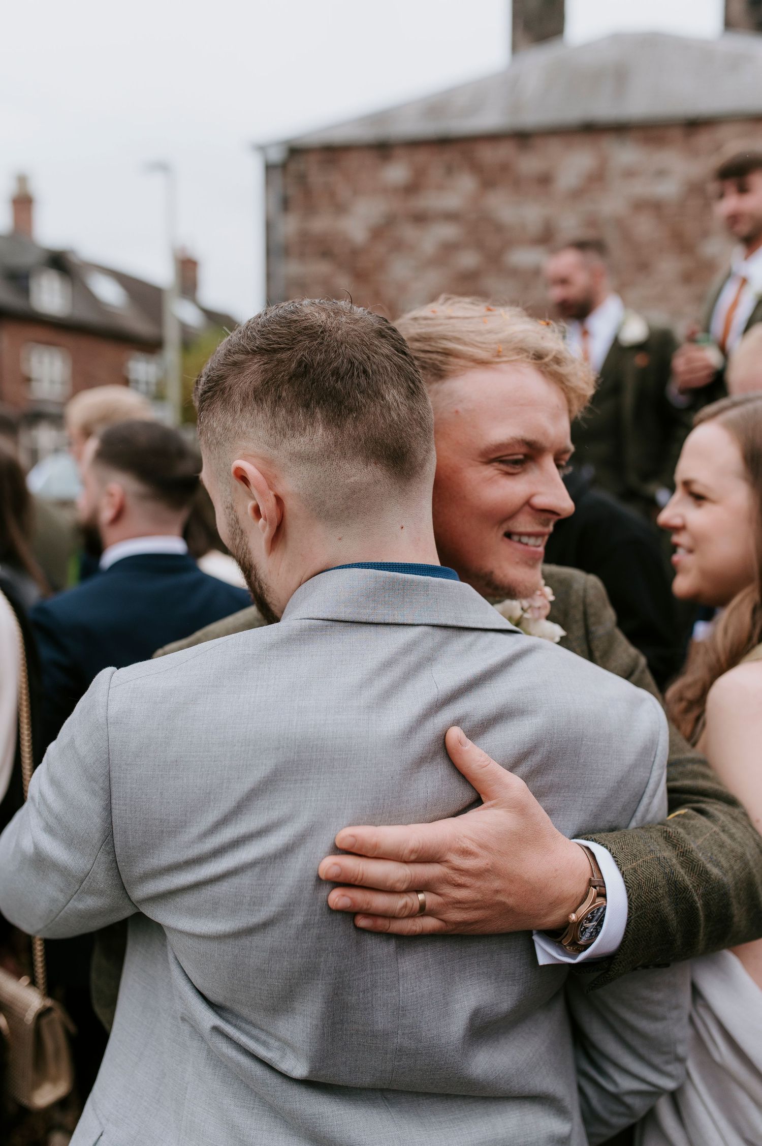 Two people share a warm embrace at an outdoor gathering while wearing formal attire.