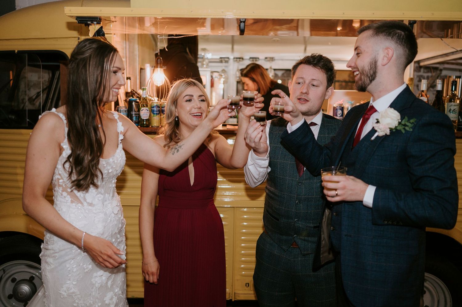 Bride and wedding guests enjoy drinks together at a vintage yellow bar cart at the reception.