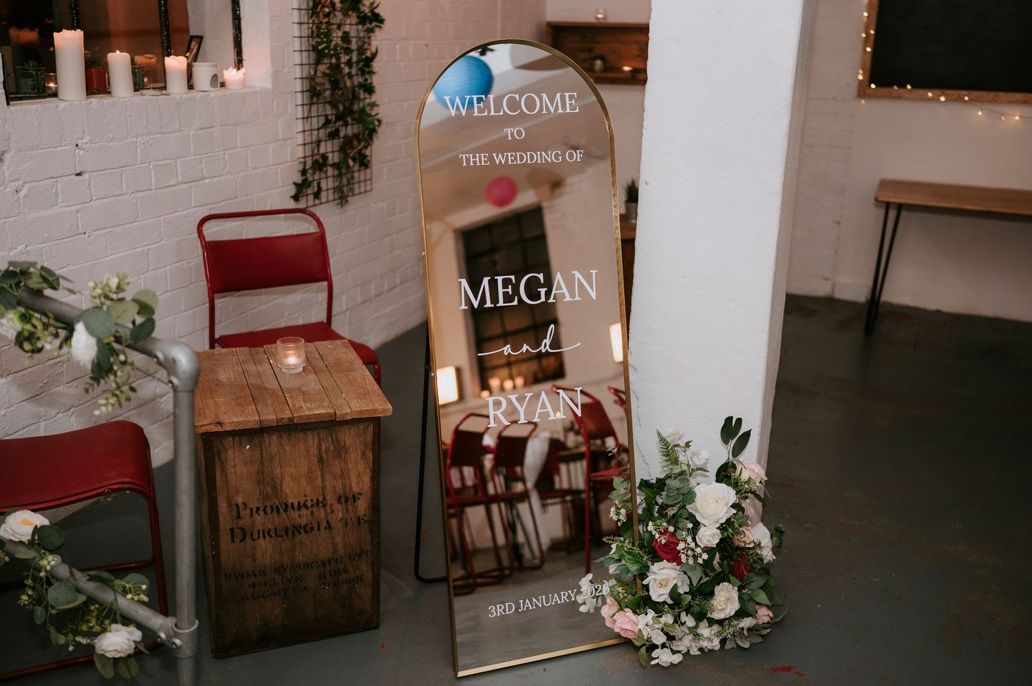 Mirror wedding welcome sign for Megan and Ryan decorated with florals at a rustic venue.