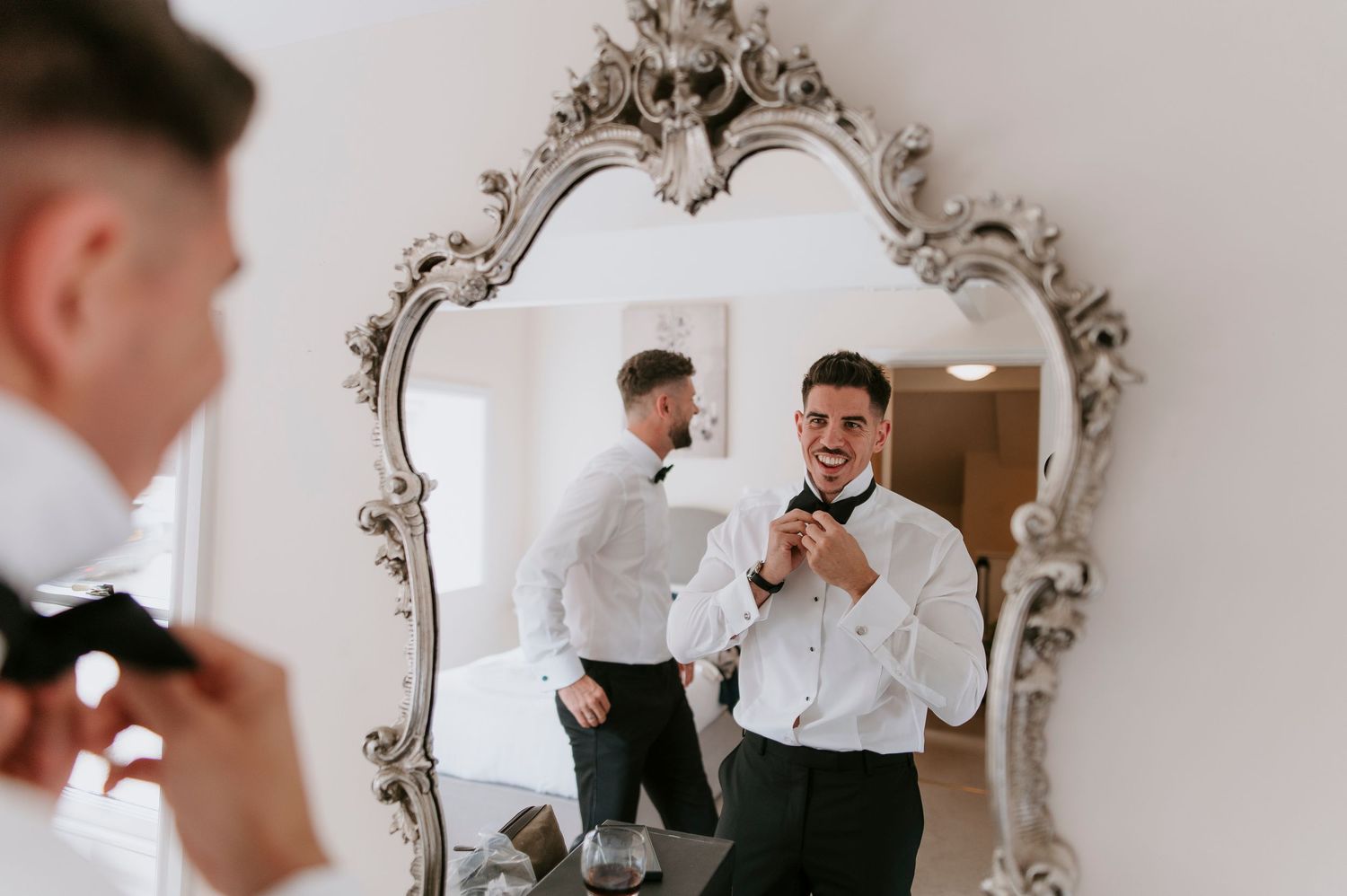 A person in a white shirt adjusts their tie while looking into an ornate silver mirror.
