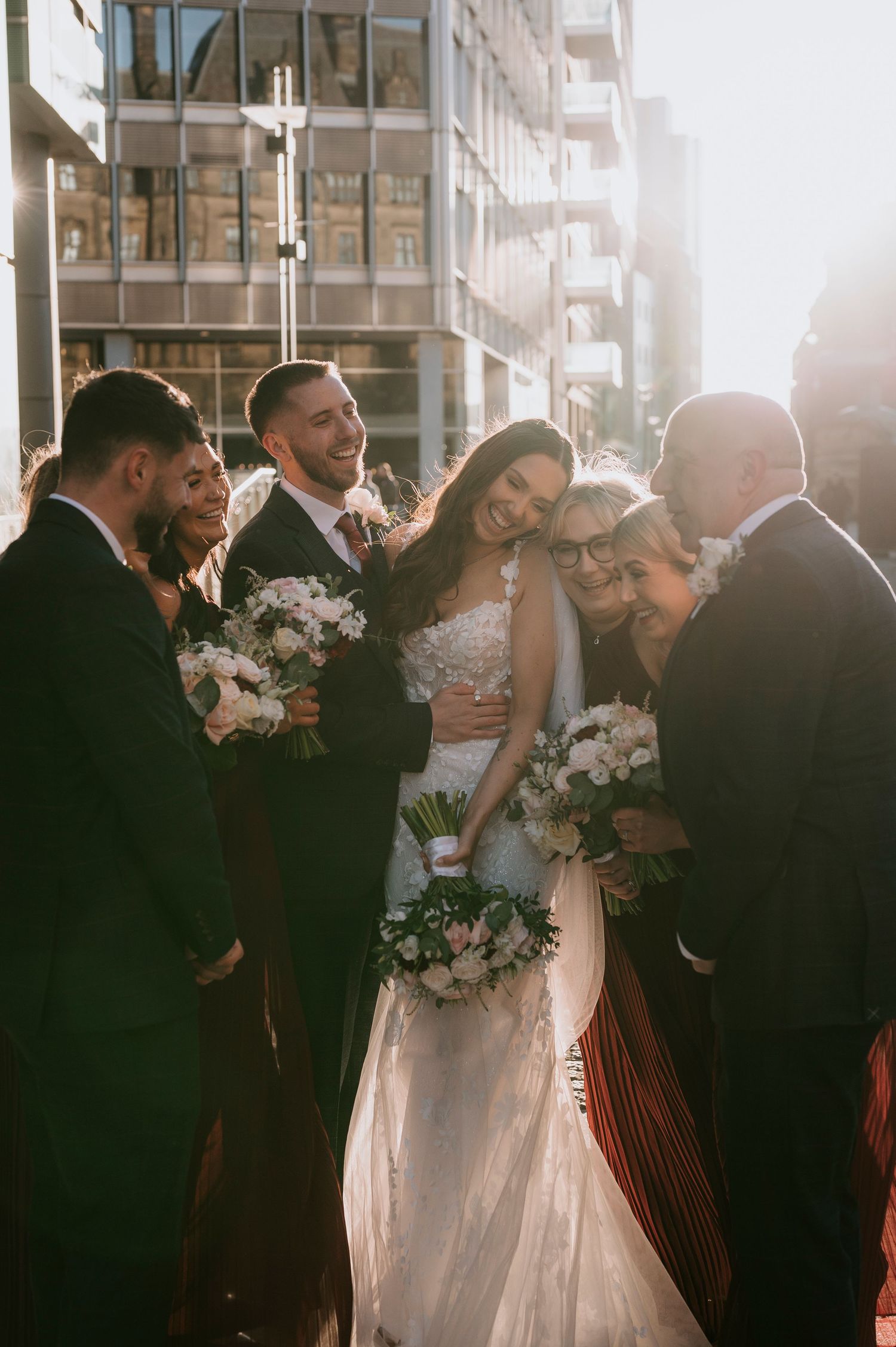 Wedding party celebrates outdoors in warm sunlight with elegant white floral bouquets and formal attire.