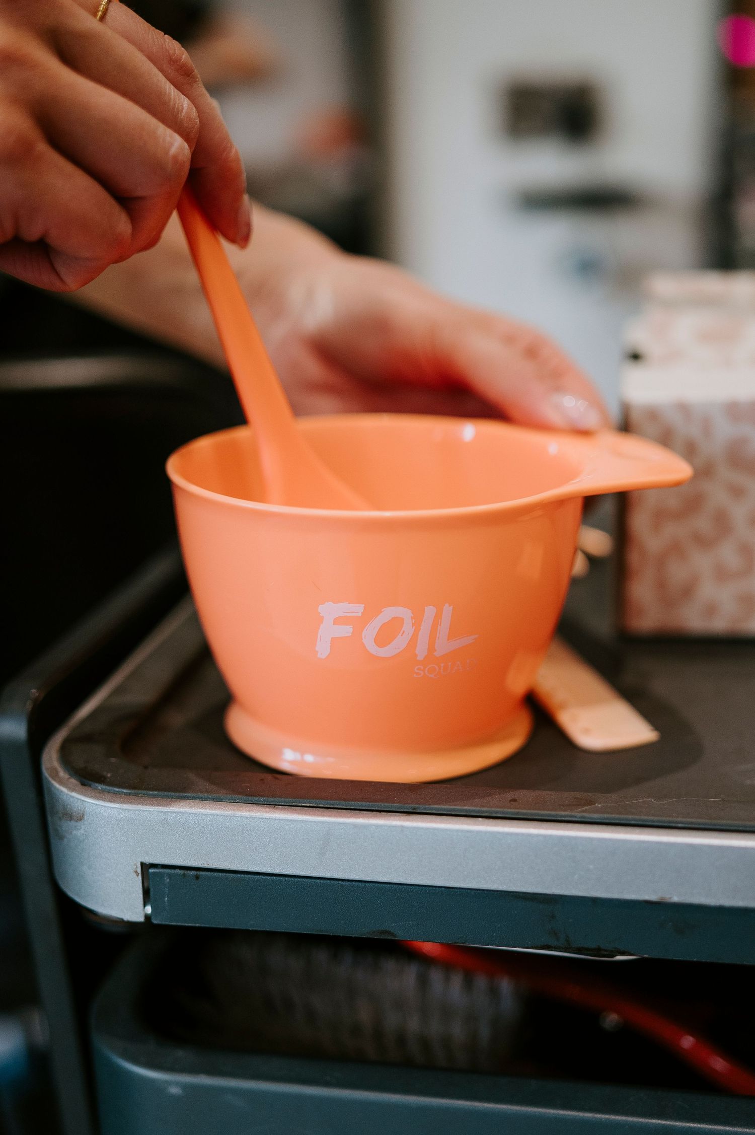 A coral-colored mixing bowl with FOIL branding being used with a spatula on a dark surface.
