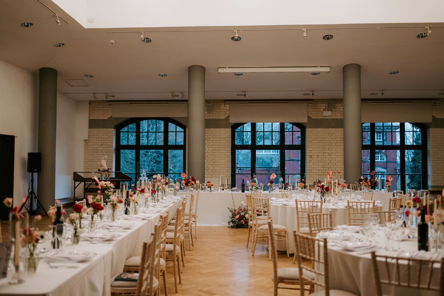 Spacious wedding reception hall with white-clothed tables and natural light streaming through tall windows.