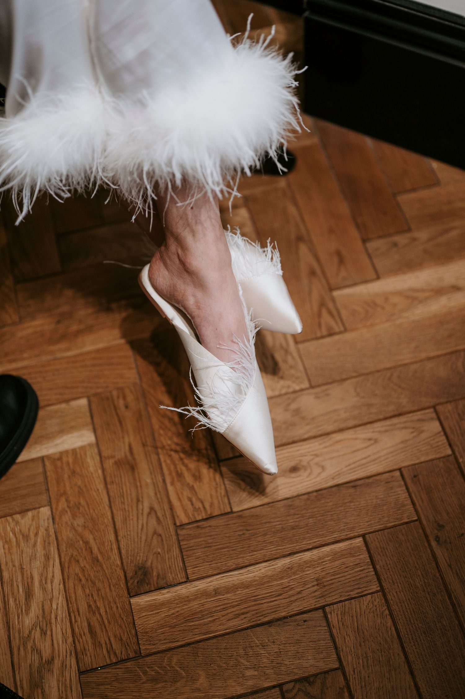 White feather-trimmed bridal shoes on herringbone wooden floor.