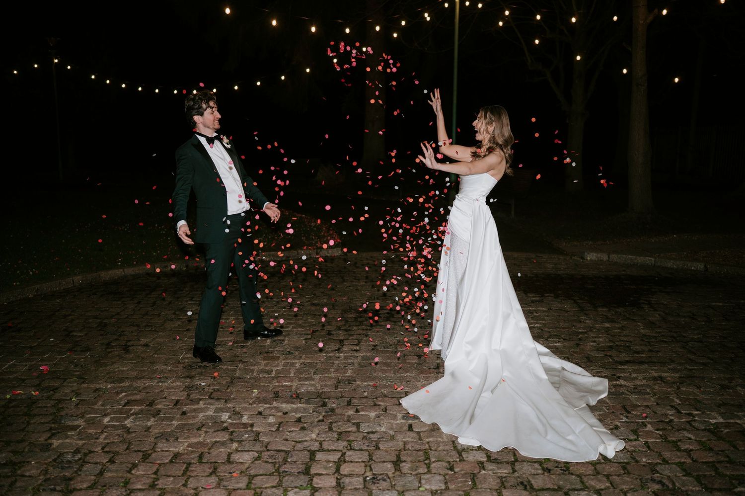 Newlyweds twirling on a rustic stone patio beneath romantic overhead string lights at dusk.