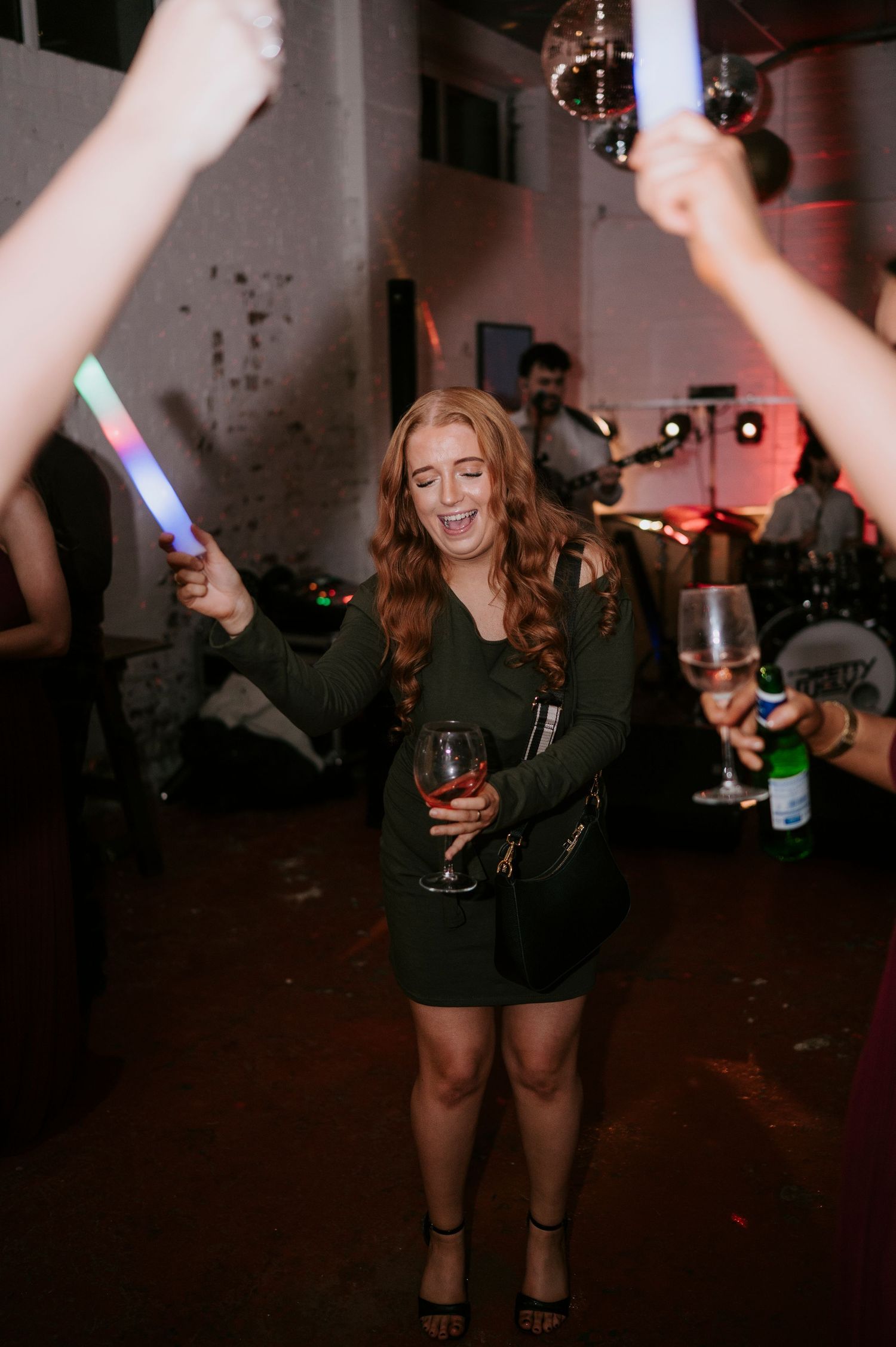 Happy wedding guest dances with a glowing LED stick and wine glass at the reception.