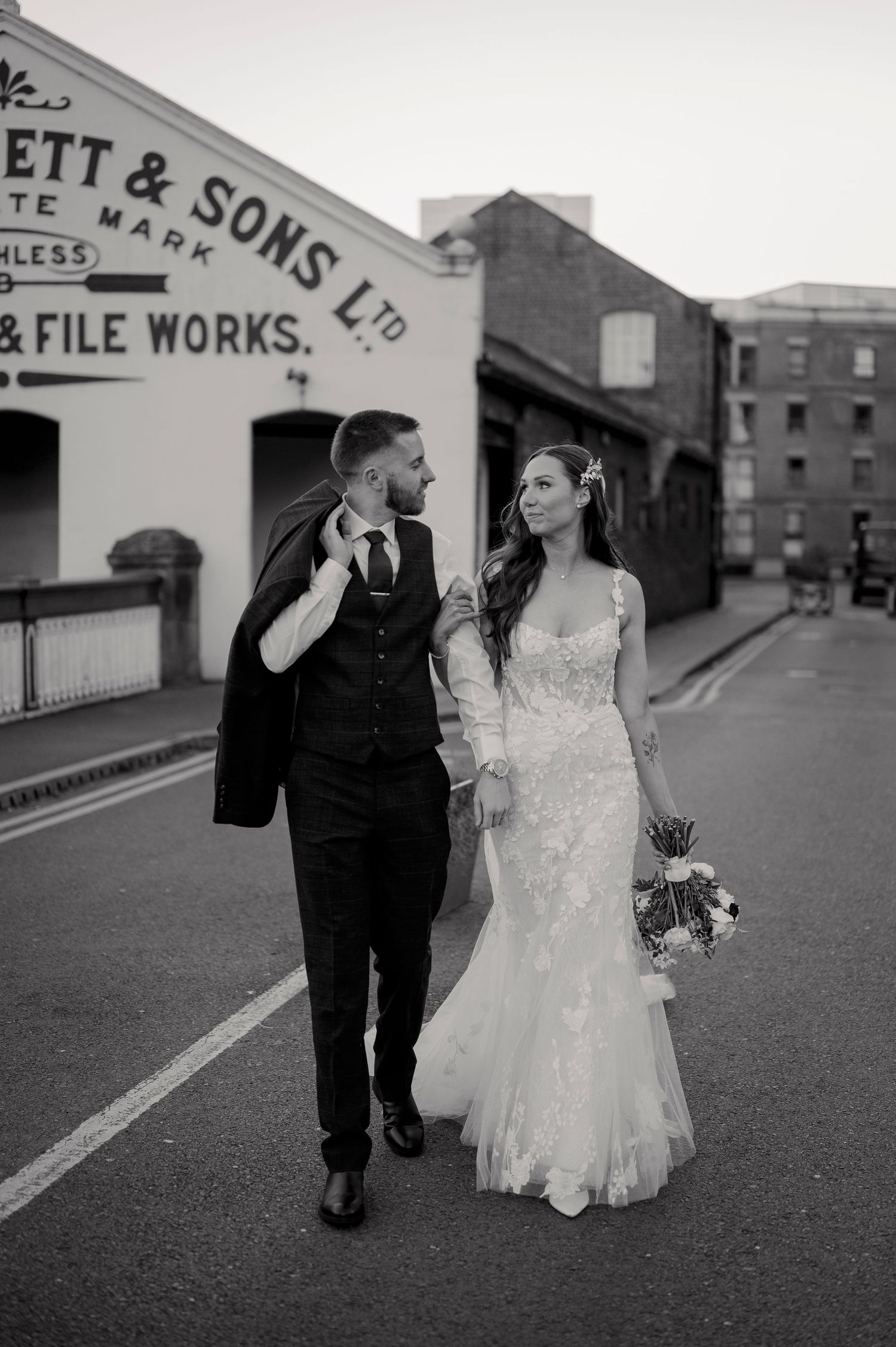 Black and white photo of bride and groom walking past historic building on their wedding day.