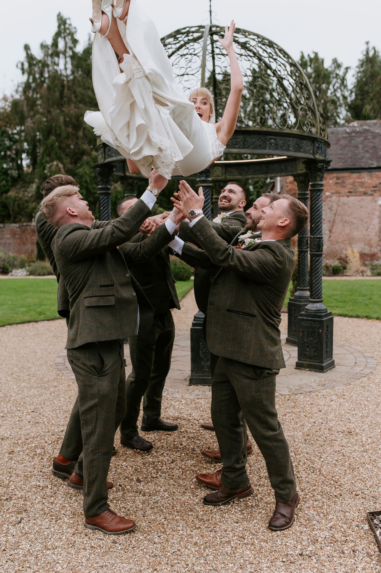 Groomsmen in dark suits playfully toss a white wedding dress into the air in a sequence of candid outdoor photos.