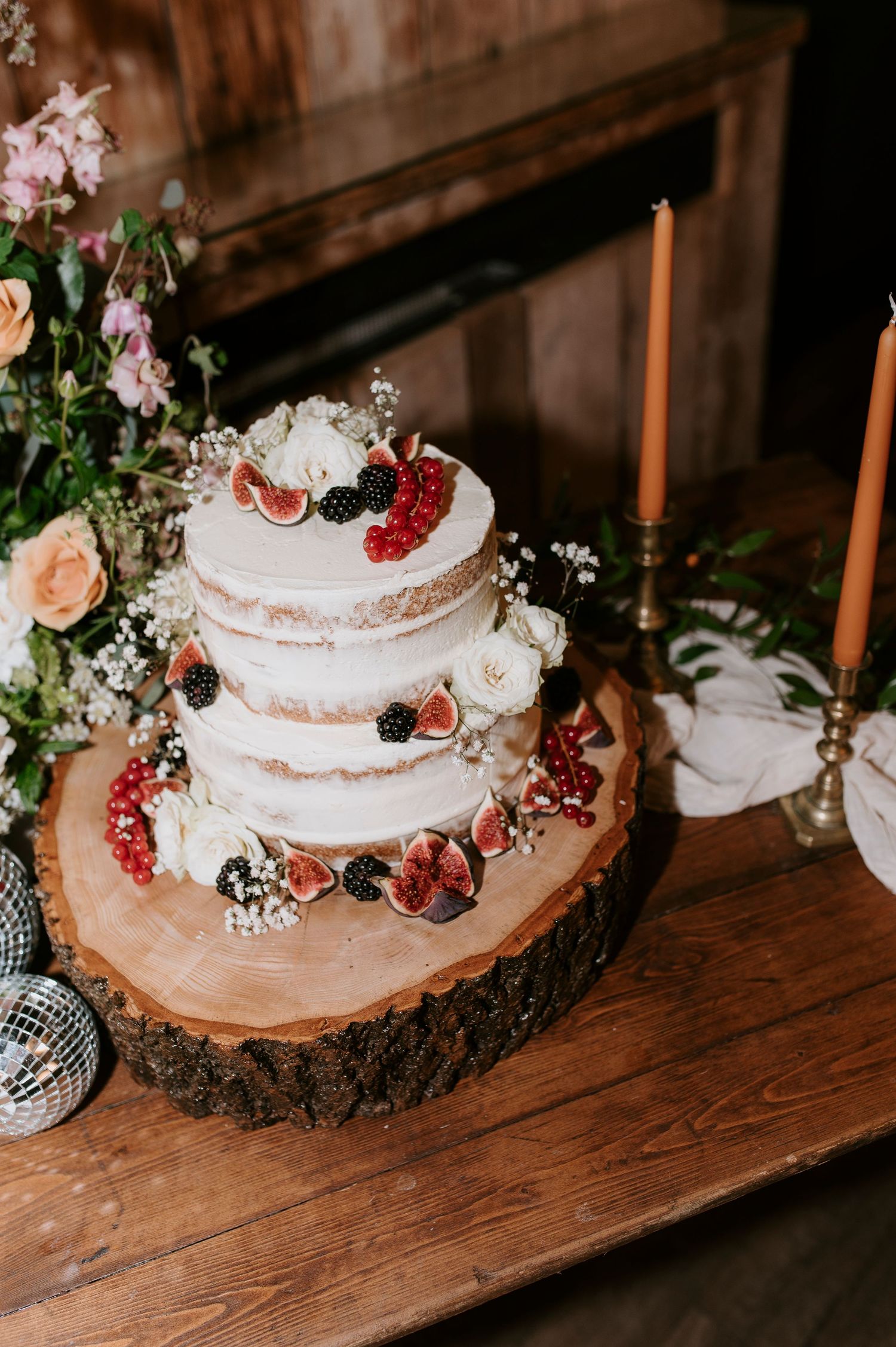 Rustic wedding cake display featuring naked cakes decorated with fresh berries on wooden slices with candlesticks.