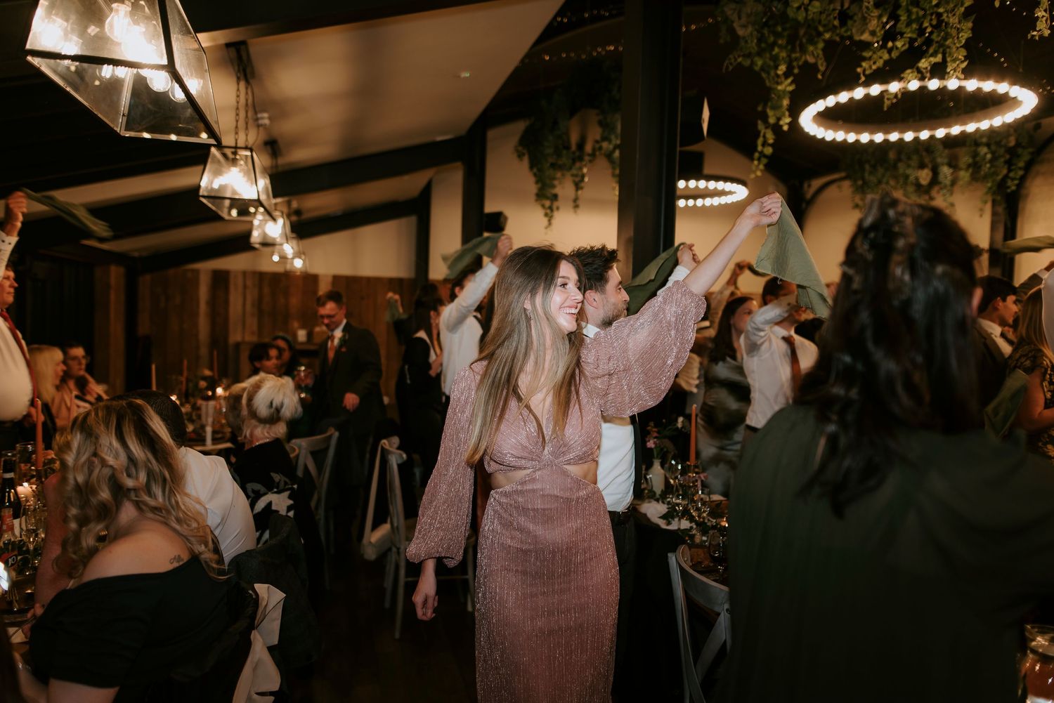 Wedding guests dance and celebrate on a dimly lit dance floor during an evening reception.