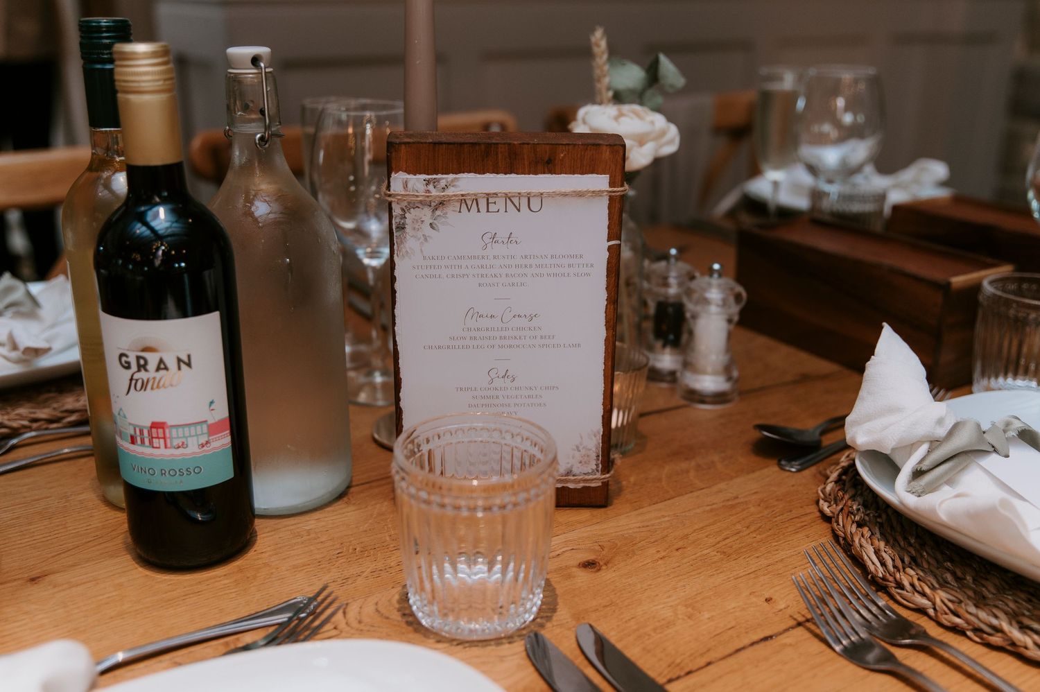 A collection of wine bottles and place settings arranged on a rustic wooden dining table at a restaurant.