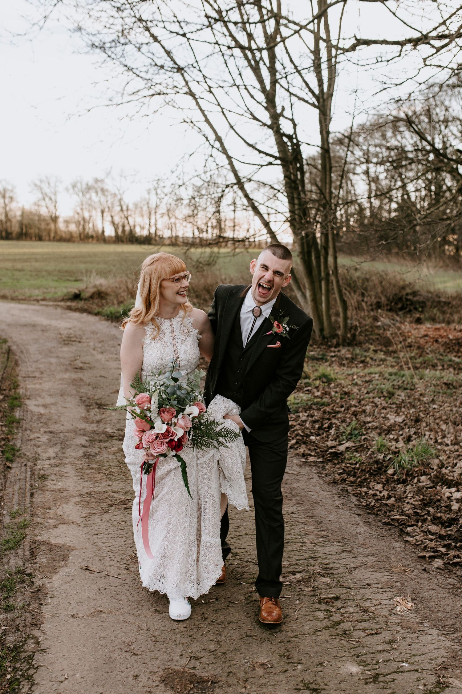 Couple walks along a winding dirt path surrounded by bare winter trees.