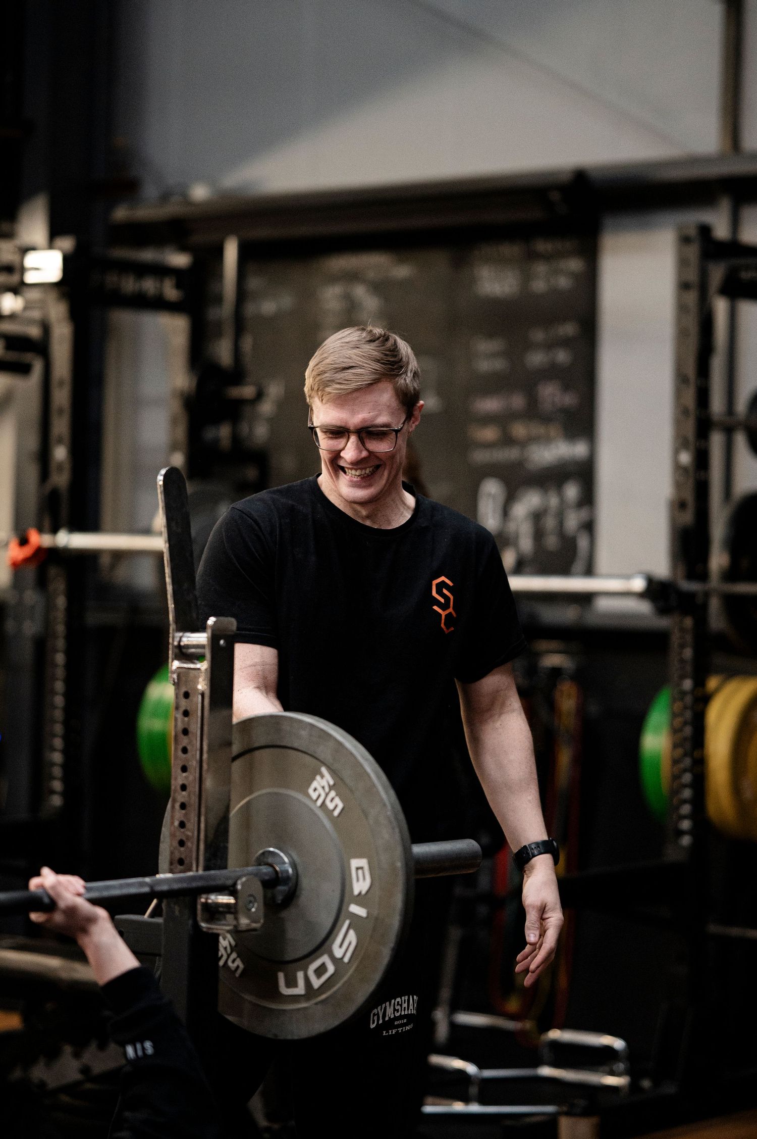 Person in black shirt lifting weights in a dimly lit gym with industrial-style brick walls and equipment.