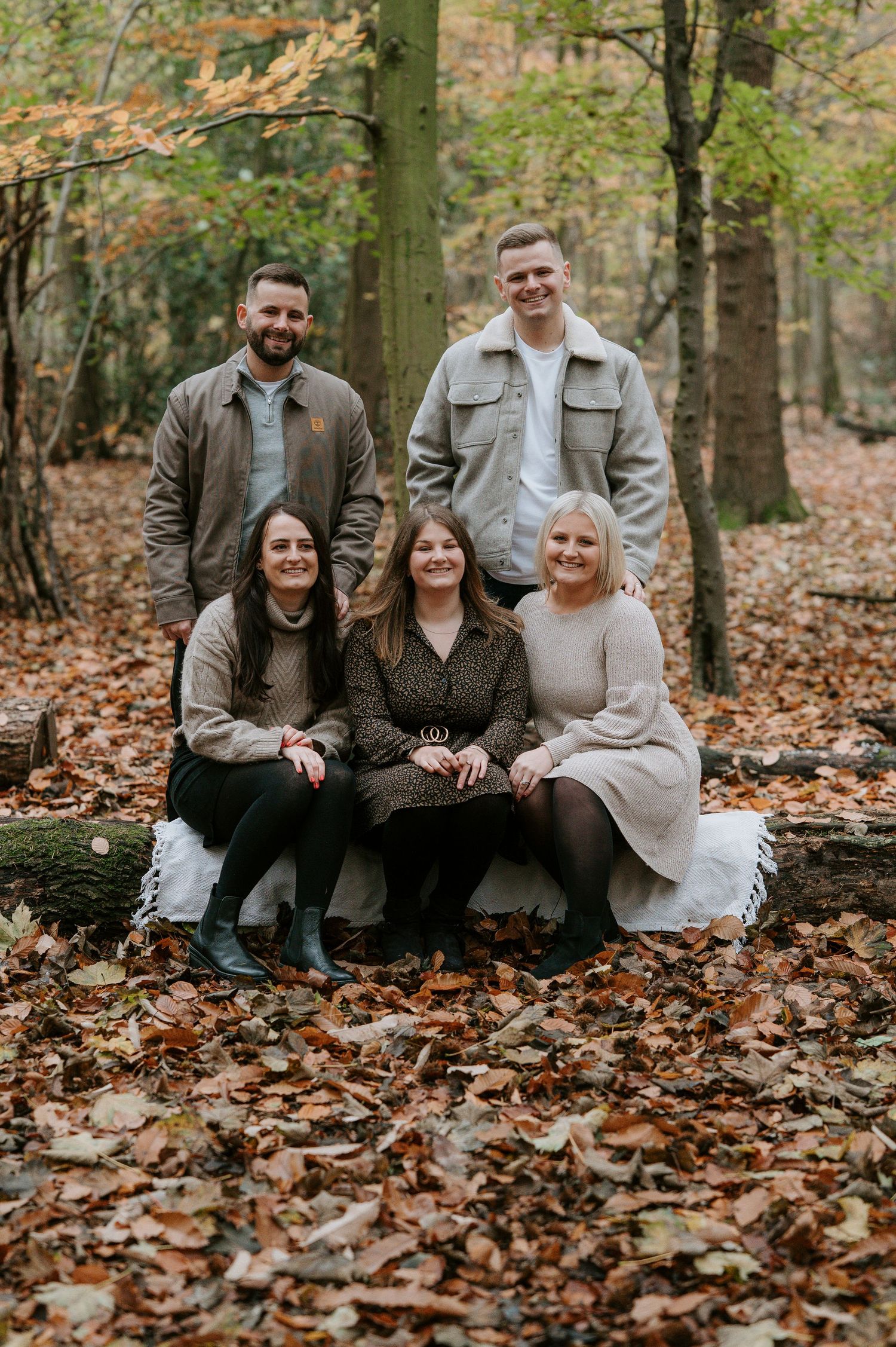 Family sitting together on fallen autumn leaves in a forest during outdoor photo session.