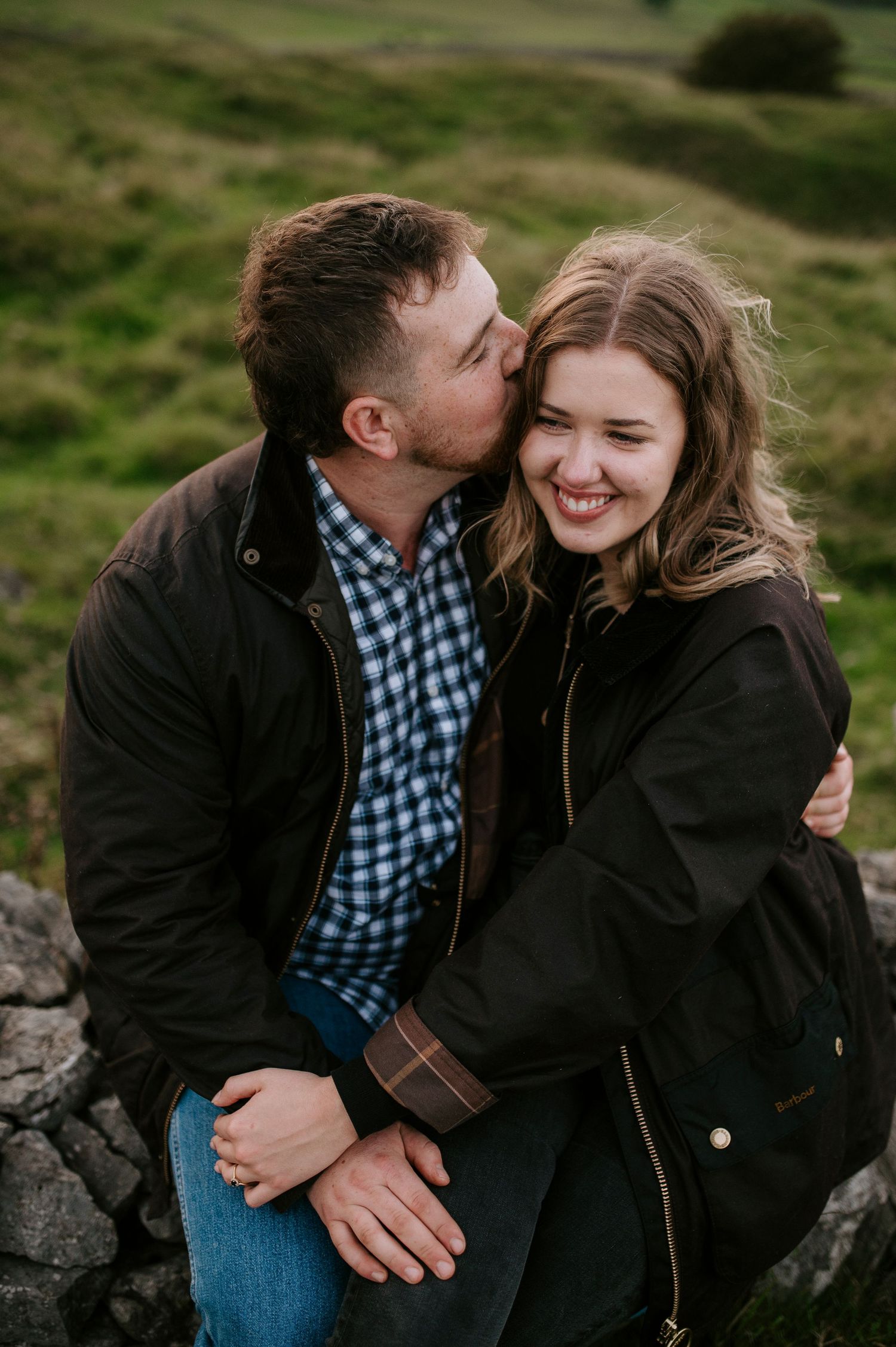 A couple shares tender moments together while sitting on rocks in a green outdoor setting.