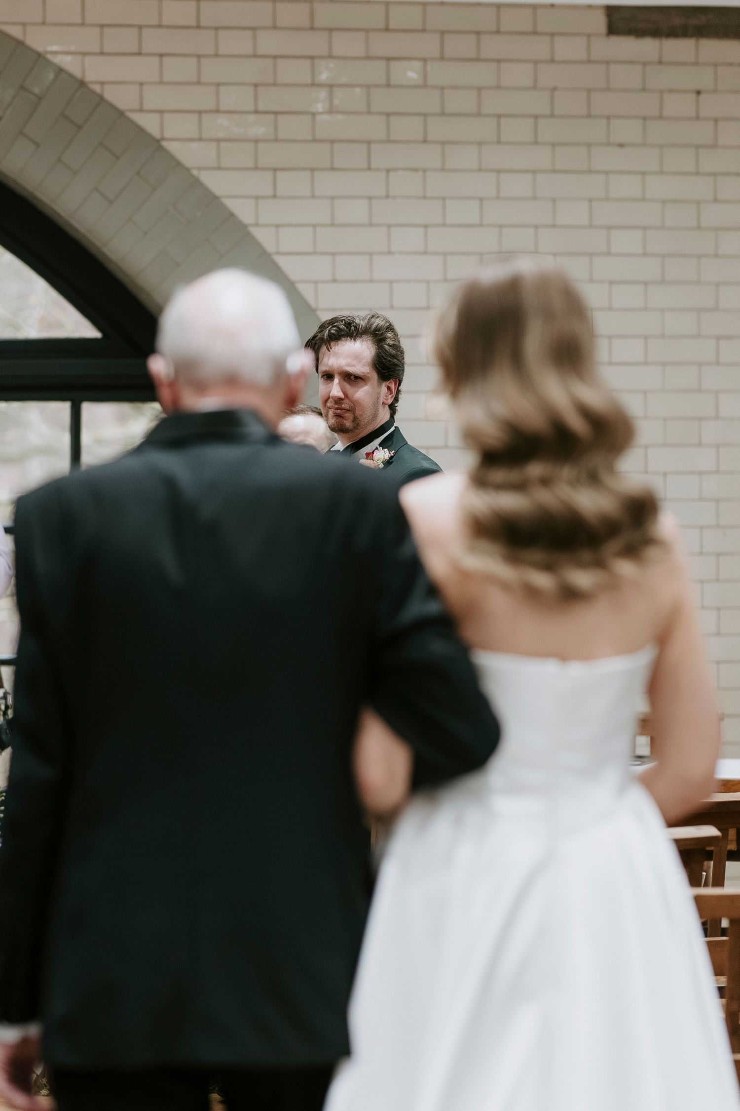 Wedding ceremony participants walk down church aisle with brick walls visible in background.