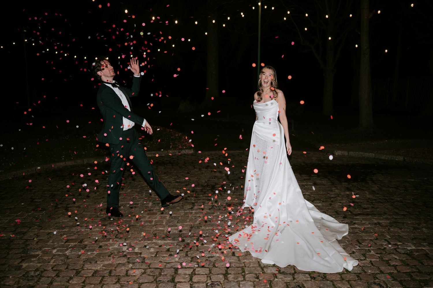 Wedding couple dances in a romantic outdoor setting as rose petals fall around them in the evening light.