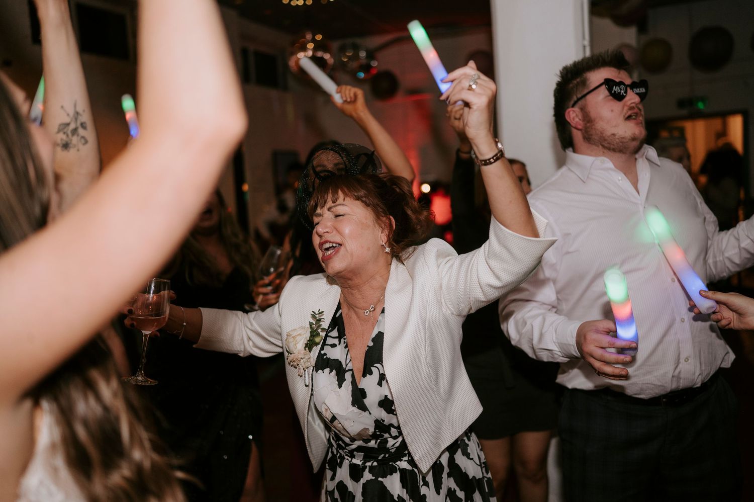 Wedding guests dancing energetically with colorful glow sticks at a lively reception party.