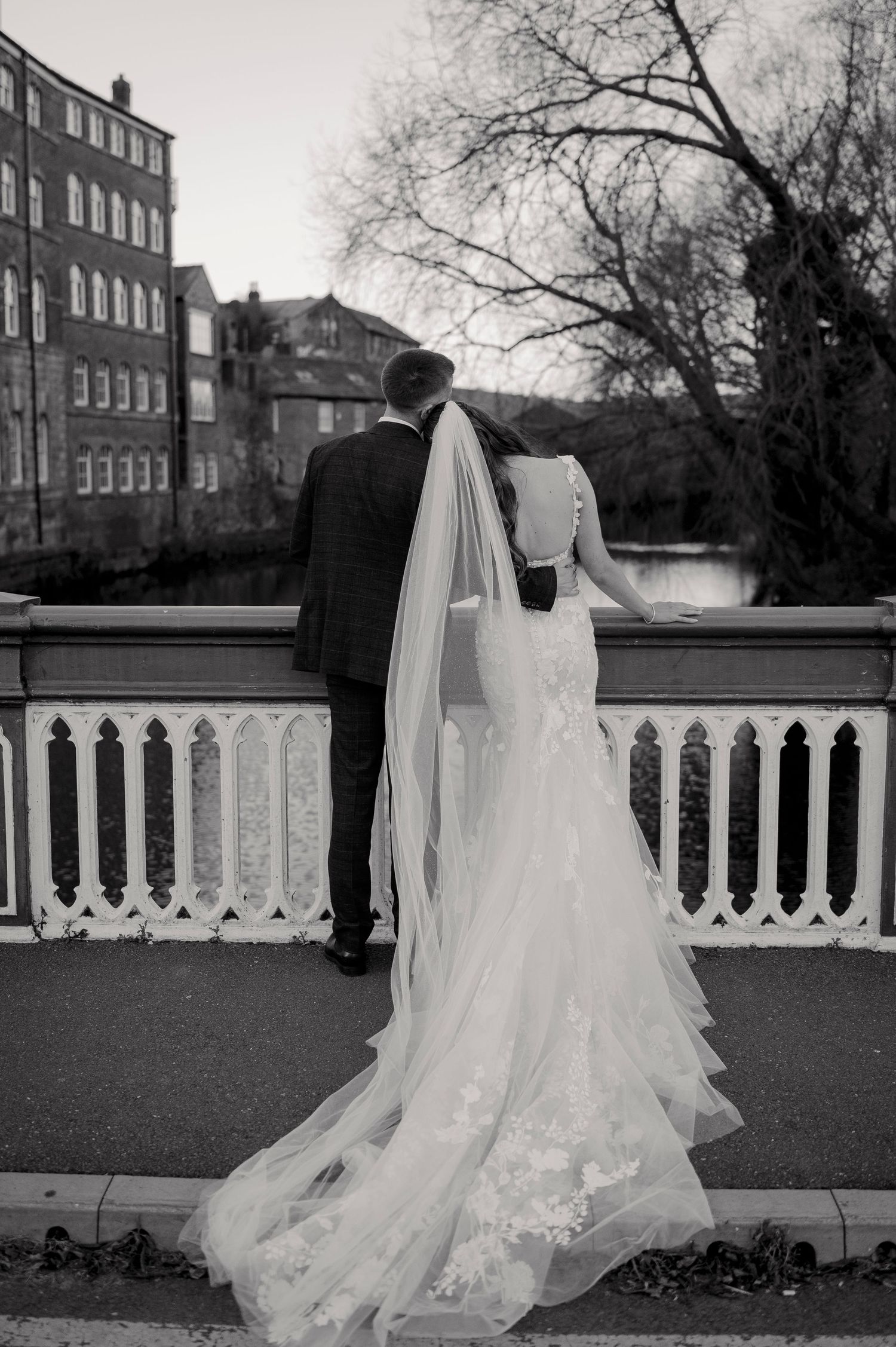Bride and groom standing on ornate bridge, bride wearing lace gown with long veil.