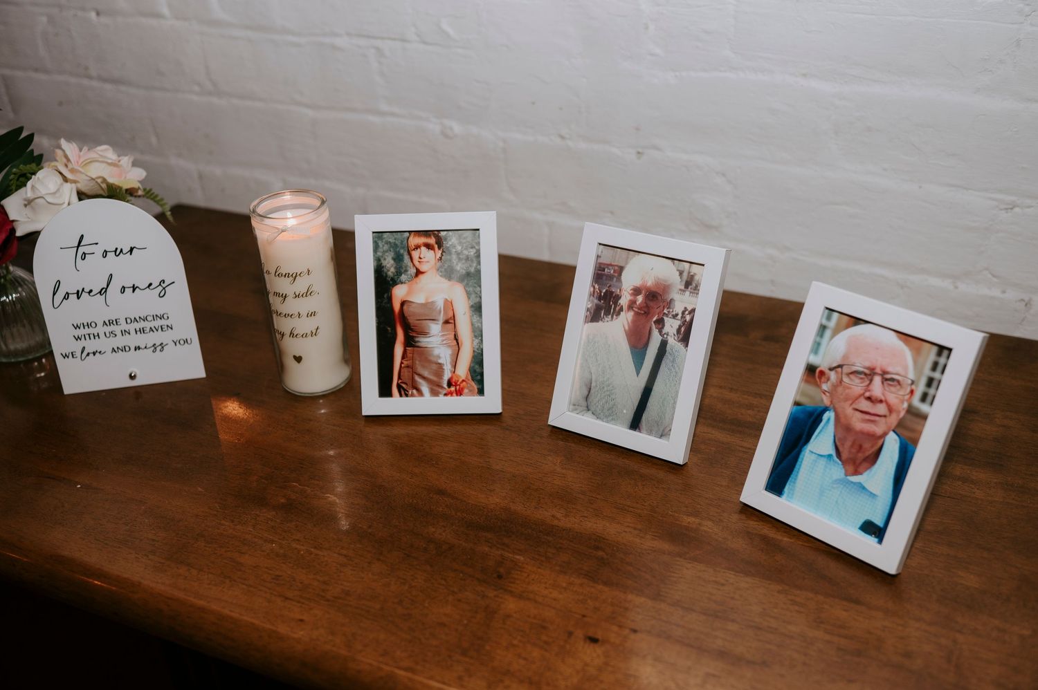 Wedding memorial table with candle, framed photos, and loving tribute sign honoring deceased loved ones.