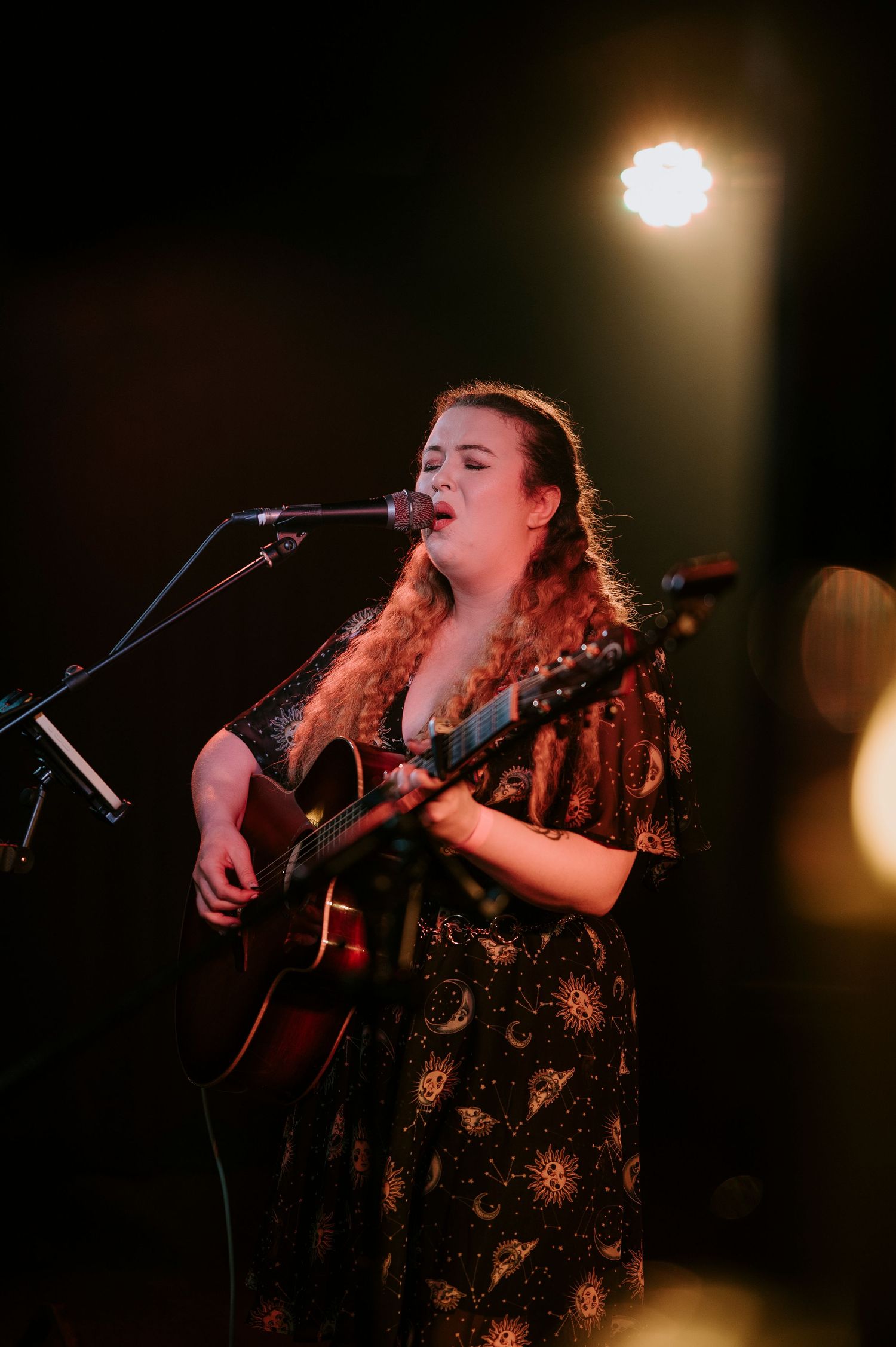 Singer performs passionately on stage with acoustic guitar under dramatic lighting at a live music venue.
