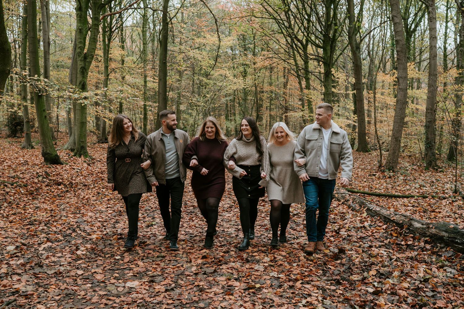 Family group portrait in a wooded area with autumn leaves scattered on the forest floor.