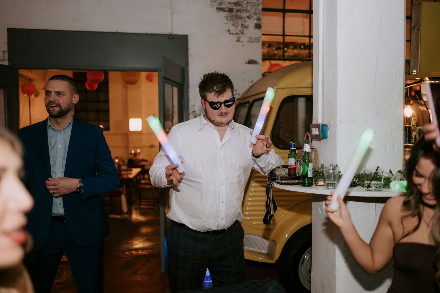 Wedding guest dancing energetically with glowsticks at lively indoor wedding reception celebration.