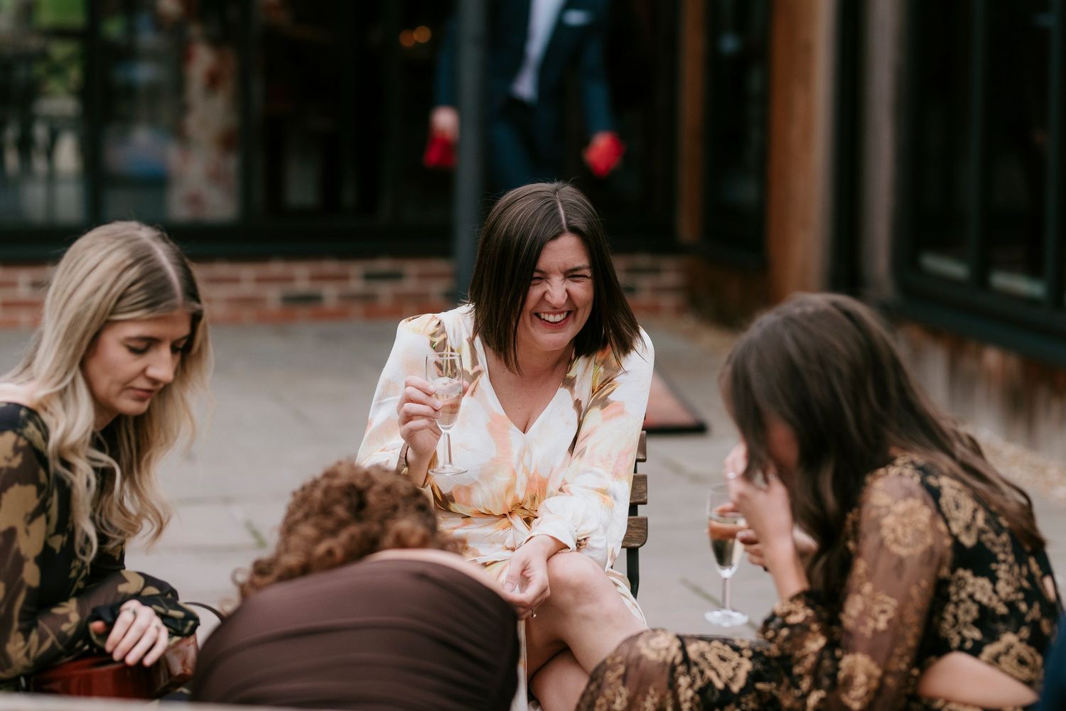 A group of people laughing and socializing at an outdoor gathering while holding drinks and snacks.
