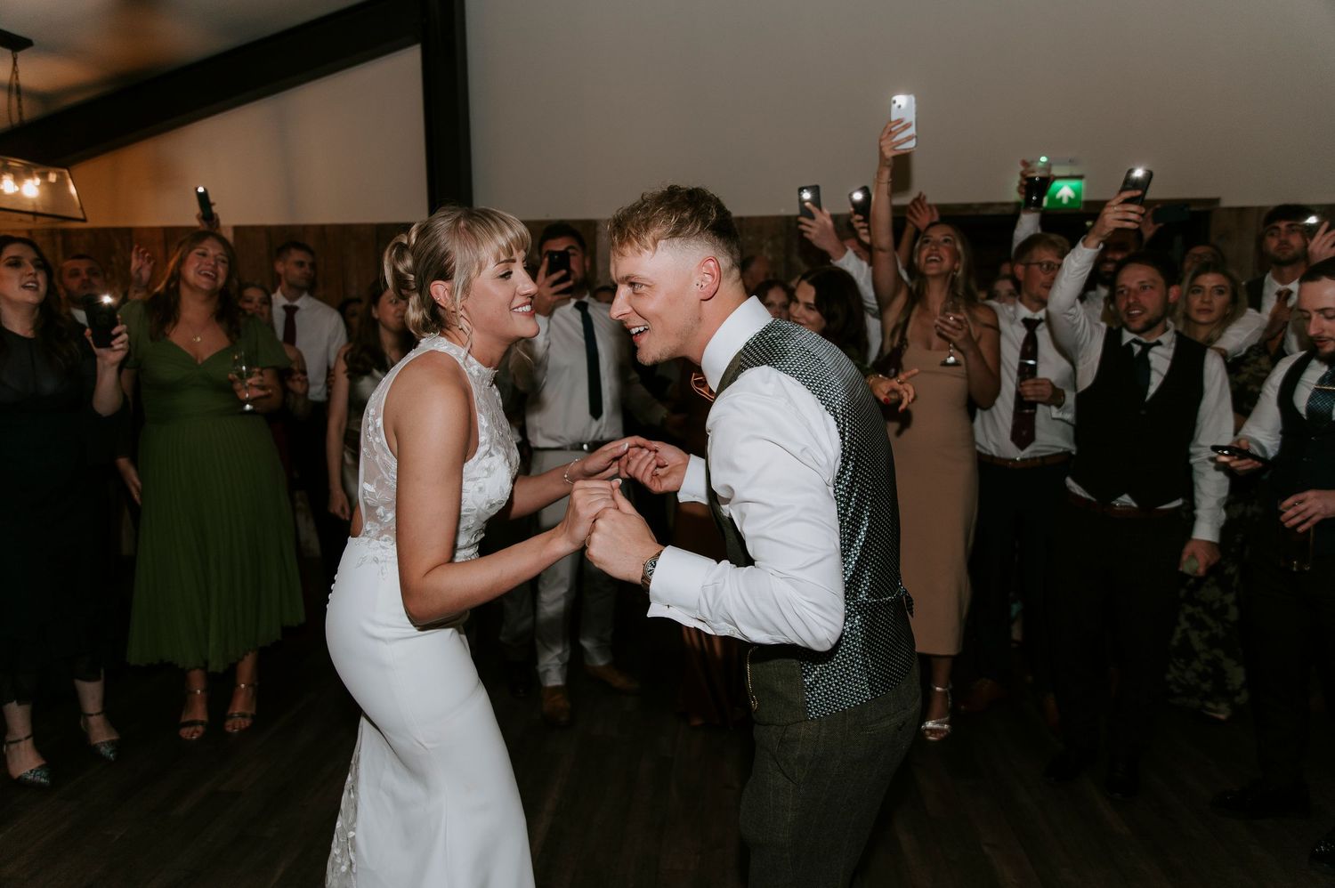 Couples dancing together at a dimly lit wedding reception venue with guests mingling in the background.