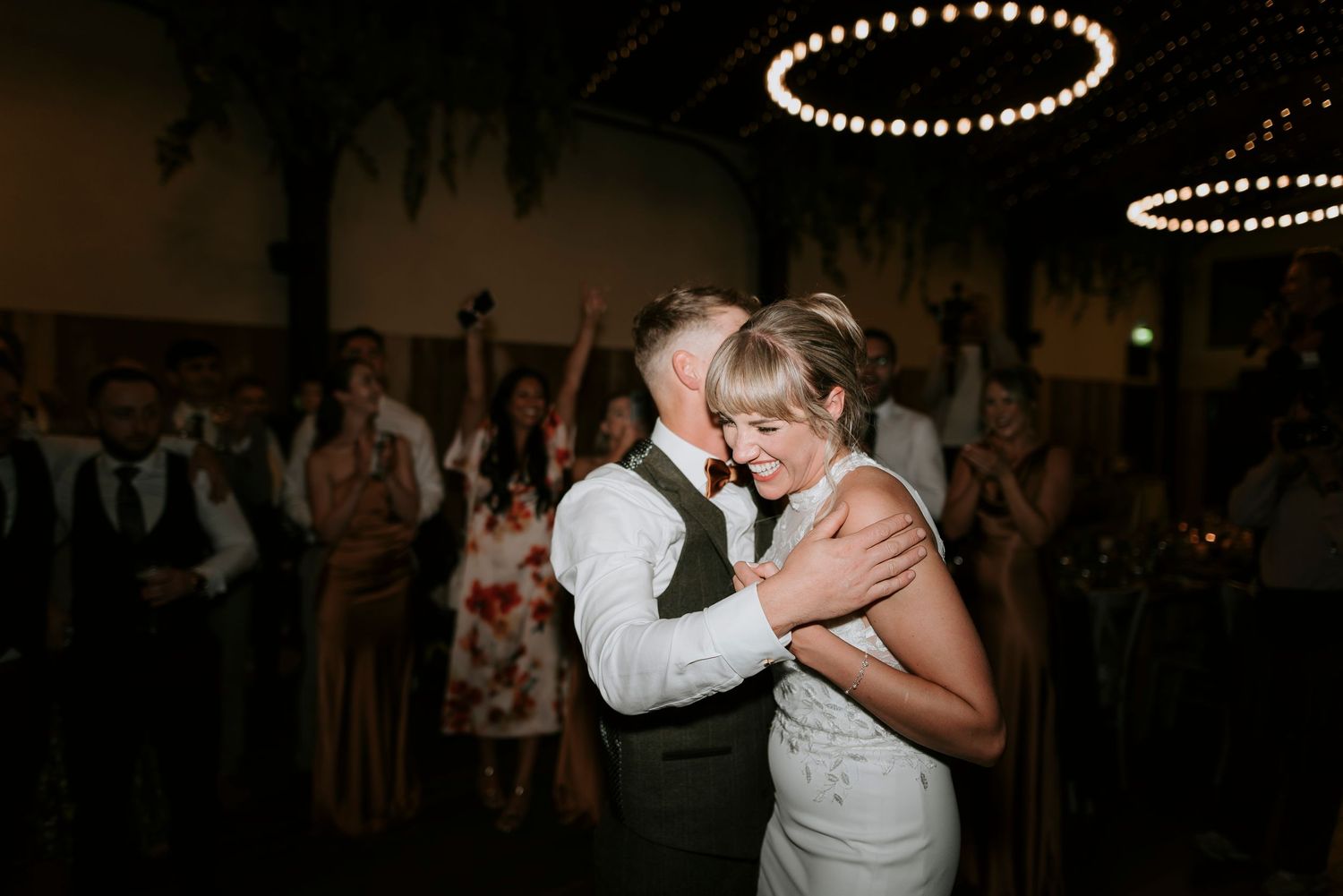 A couple shares an intimate dance moment at a wedding reception under soft lighting.