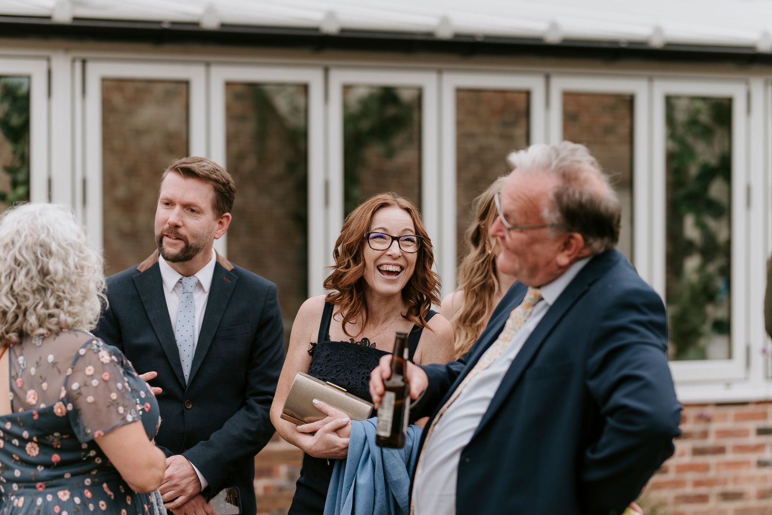 Wedding guests share joyful laughter during an outdoor reception at a brick venue.