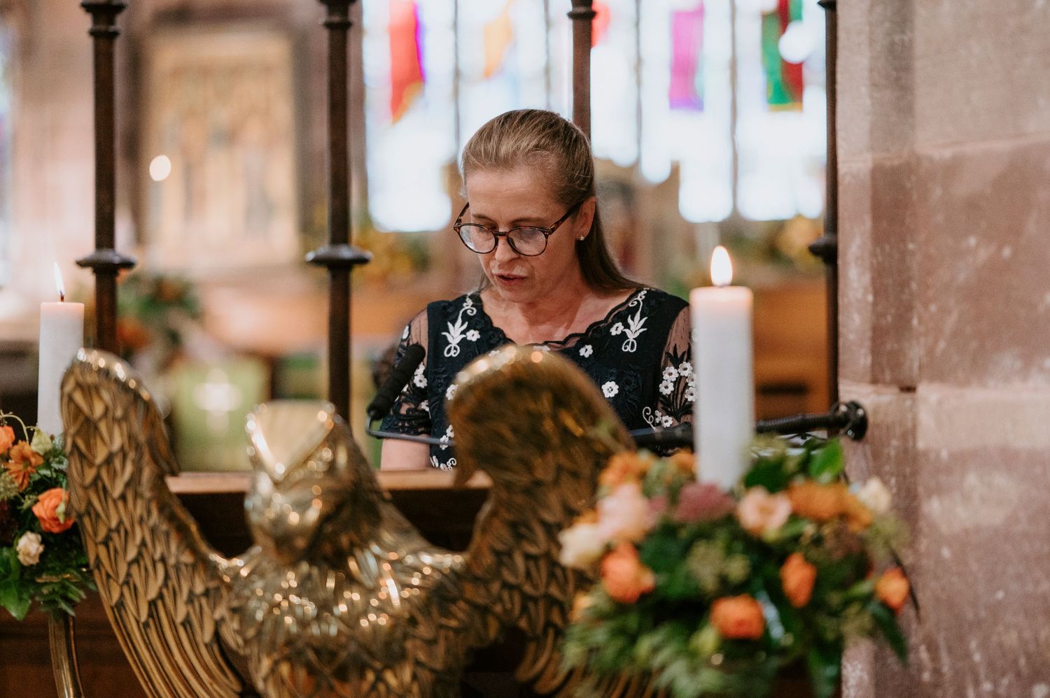 A person reads while sitting in a church pew decorated with ornate golden sculptures and floral arrangements.