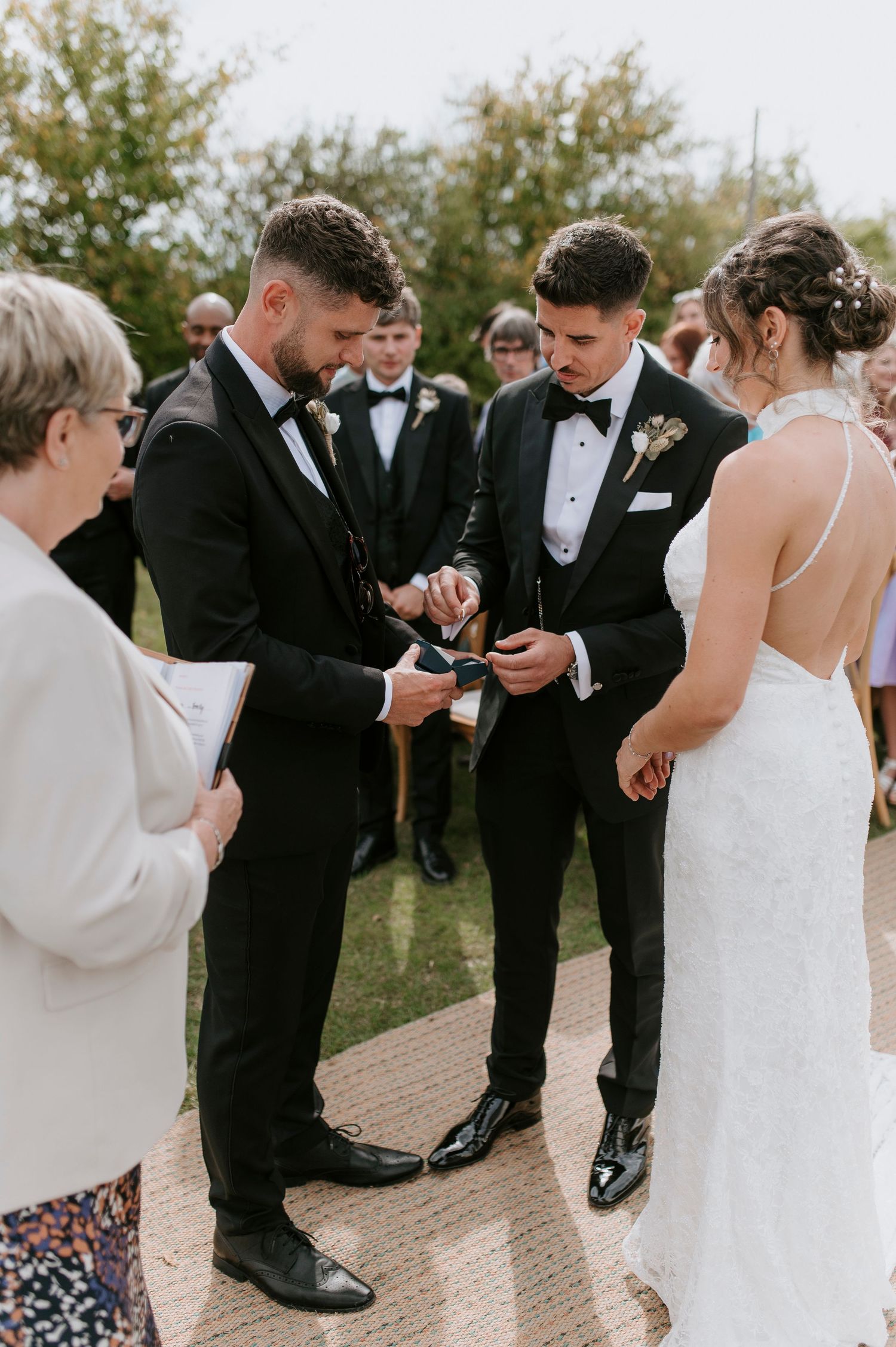 Wedding party members in formal black and white attire checking their shoes and socks during outdoor photo session.