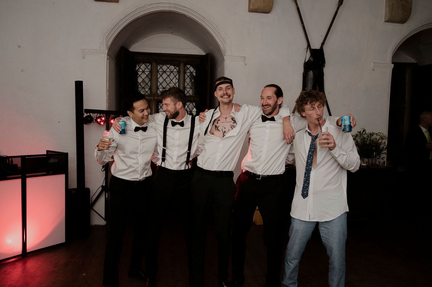 Groomsmen in suspenders and bowties posing together at a reception venue.