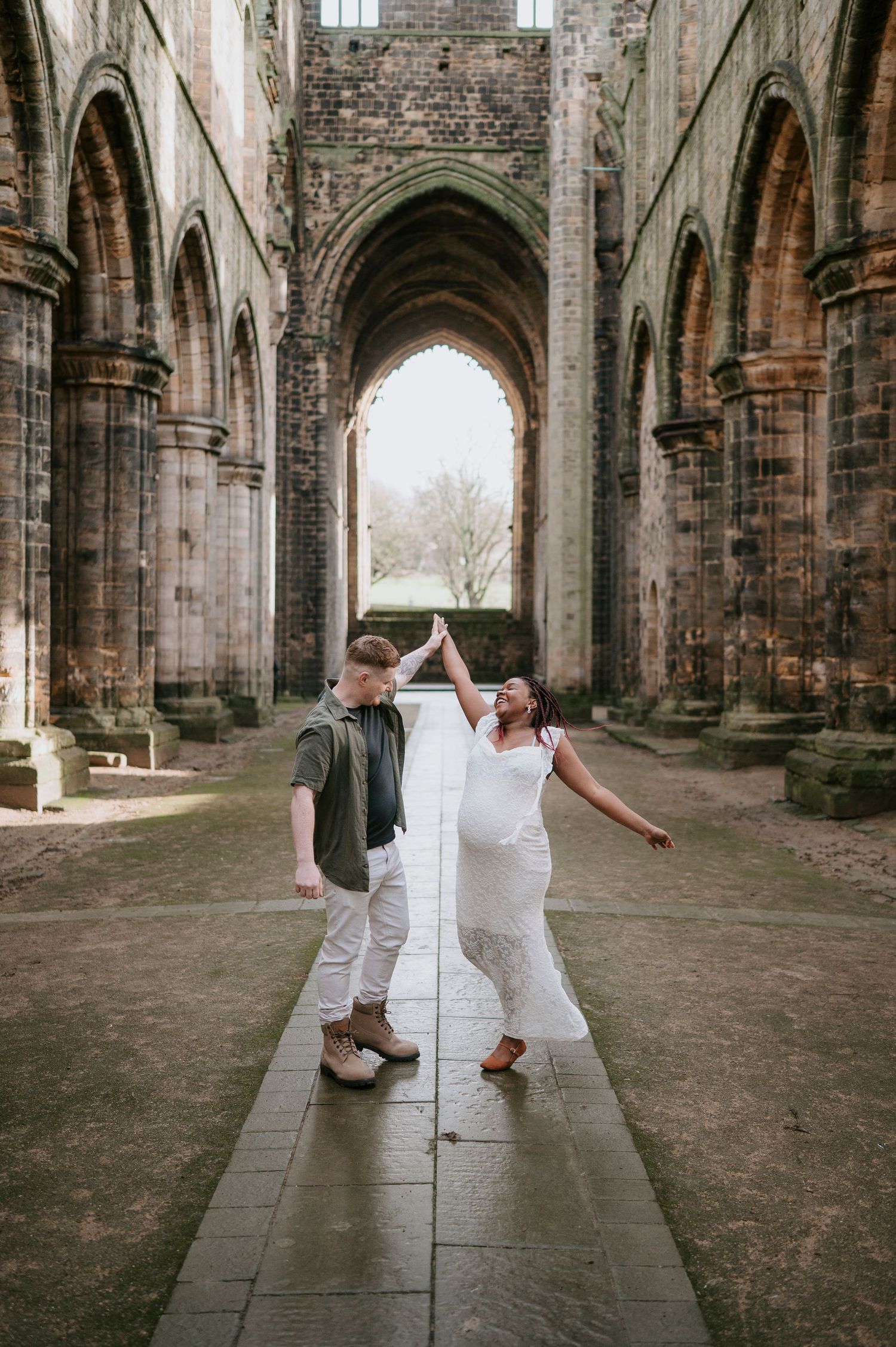 A couple dancing and celebrating in a historic stone cathedral with Gothic arches and natural lighting.