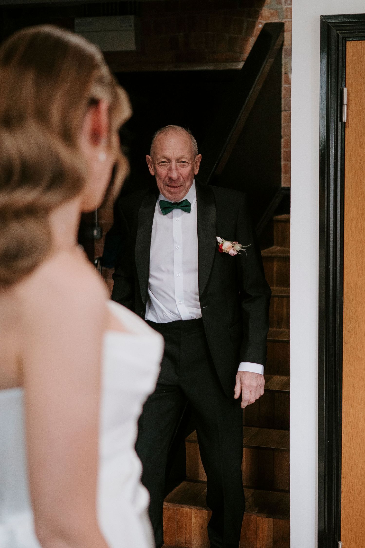 Emotional first look moment between bride and father on wooden staircase.